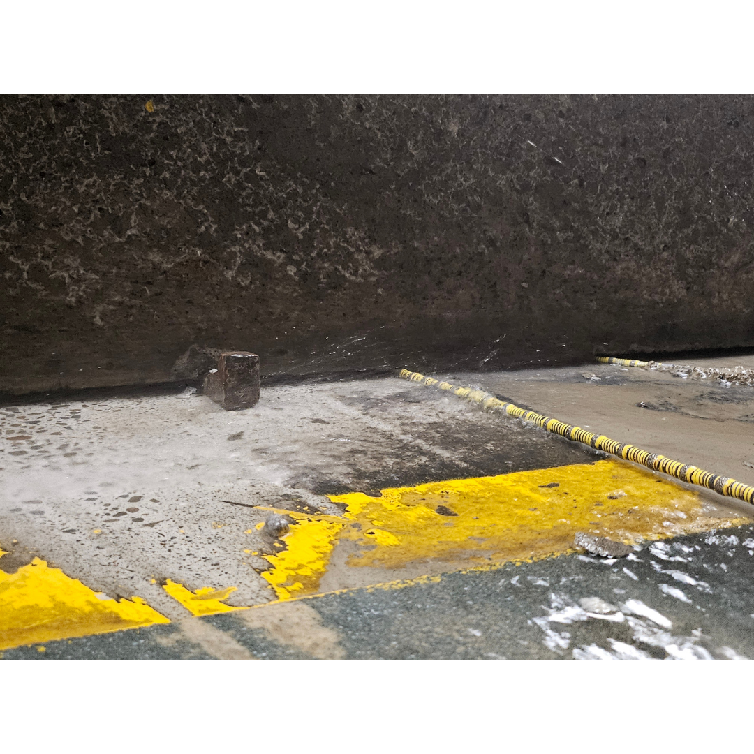 Close-up of wet, weathered concrete floor with chipped yellow paint and a small metal bolt.