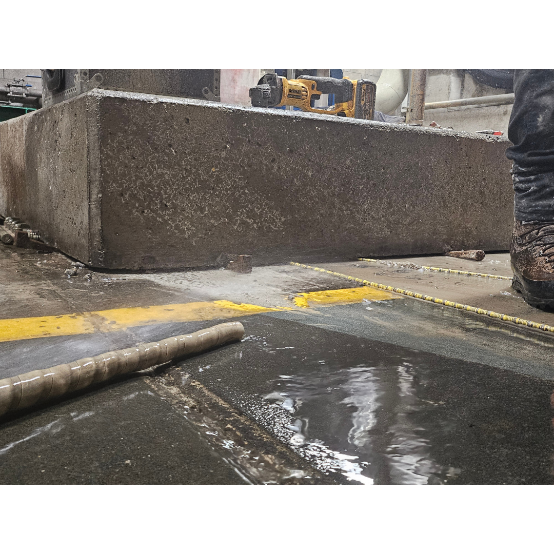 Water spraying from a hose near a concrete block and a worker's boot on a wet floor.