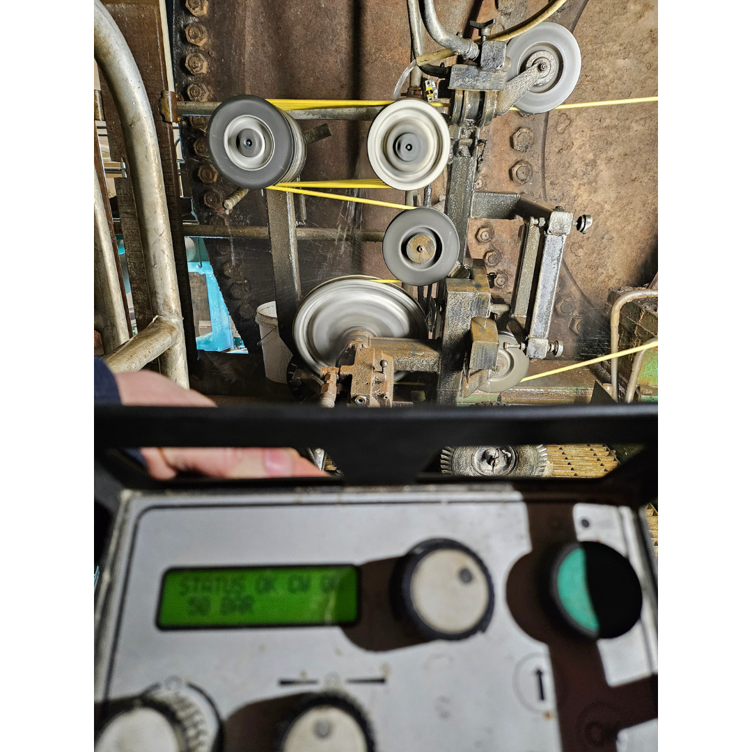 Close-up of industrial machinery with rotating pulleys and a control panel with knobs in the foreground.