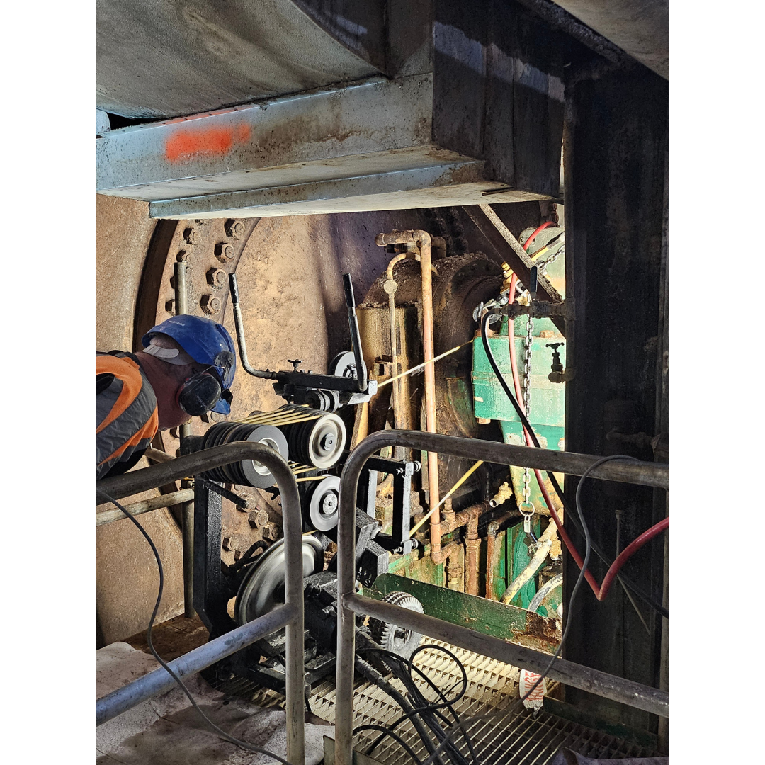 Worker with safety gear inspecting an industrial machine with pulleys and cables inside a factory.
