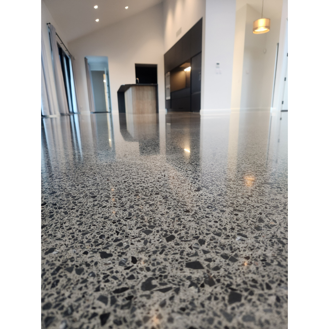 Close-up of polished terrazzo floor reflecting a modern kitchen with black cabinets and wooden island.