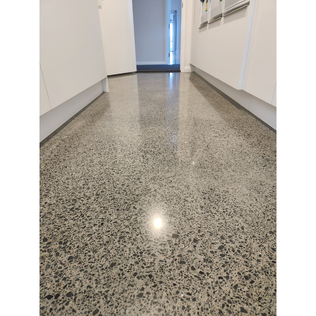 Polished speckled concrete floor in a hallway with white cabinets on both sides.