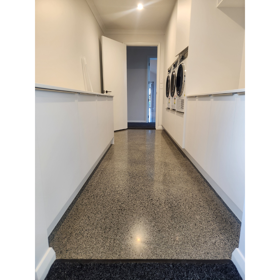 Narrow laundry room with polished concrete floor, white cabinets, and stacked washers on the right.