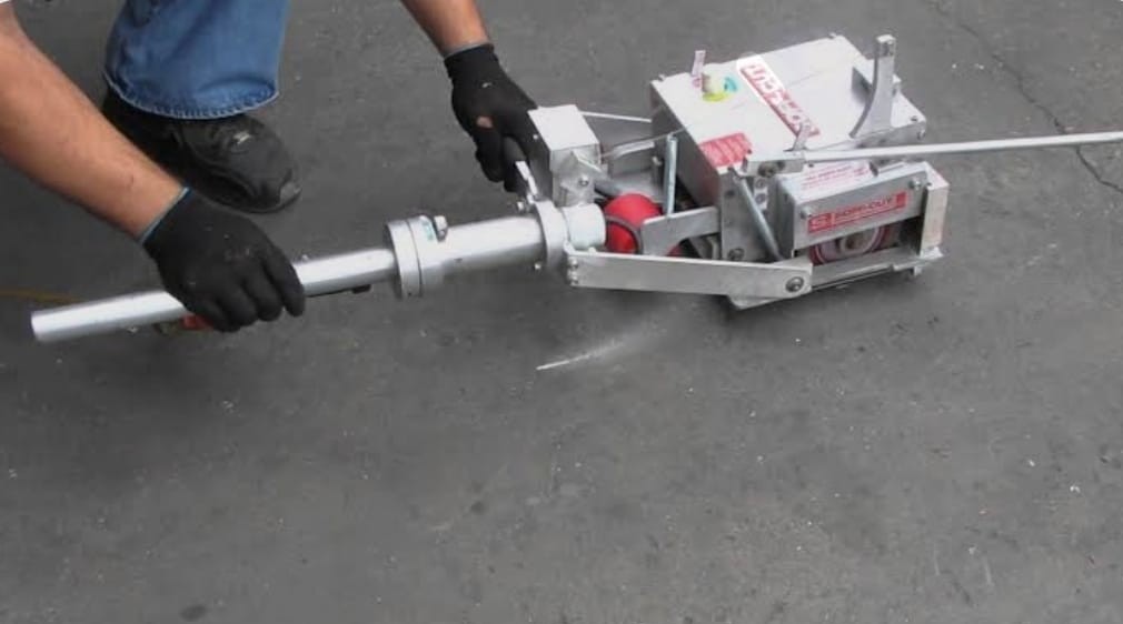 Person wearing black gloves handling a metal street marking machine on pavement.