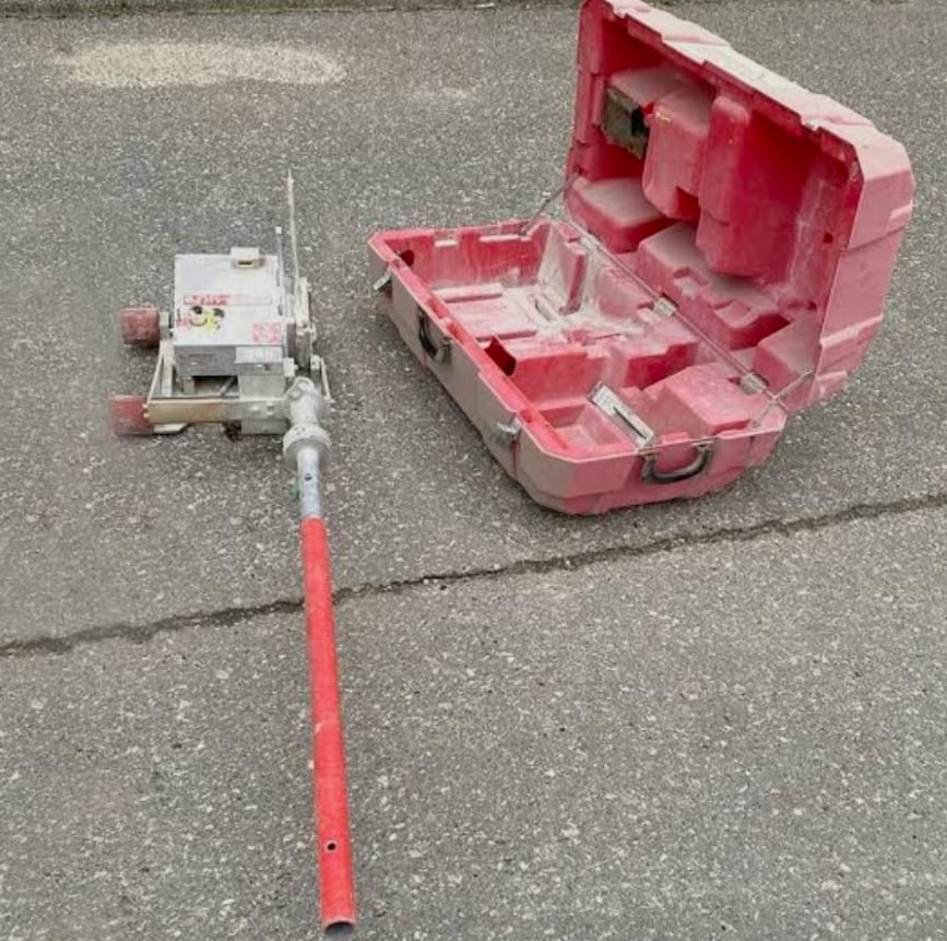 Portable concrete scanning device with red handle and open red carrying case on asphalt ground.