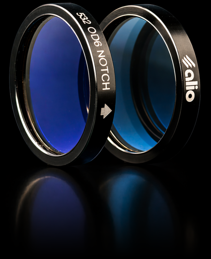 Two mounted 532 nm OD6 notch filters in black anodized housings standing upright on a reflective surface, one facing forward showing the engraved label "532 OD6 NOTCH" with a directional arrow, the other showing the deep blue interference coating and Alio Labs logo on the mount edge.