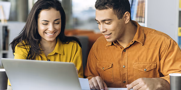 Dos jóvenes sonrientes revisando algo en una computadora portátil en un entorno interior.