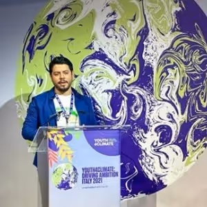 Hombre hablando en un podio con el logo de Youth4Climate y un gran globo terráqueo detrás.