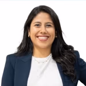 Mujer con cabello largo y oscuro, vestida con chaqueta azul y camiseta blanca, sonriendo frente a fondo blanco.
