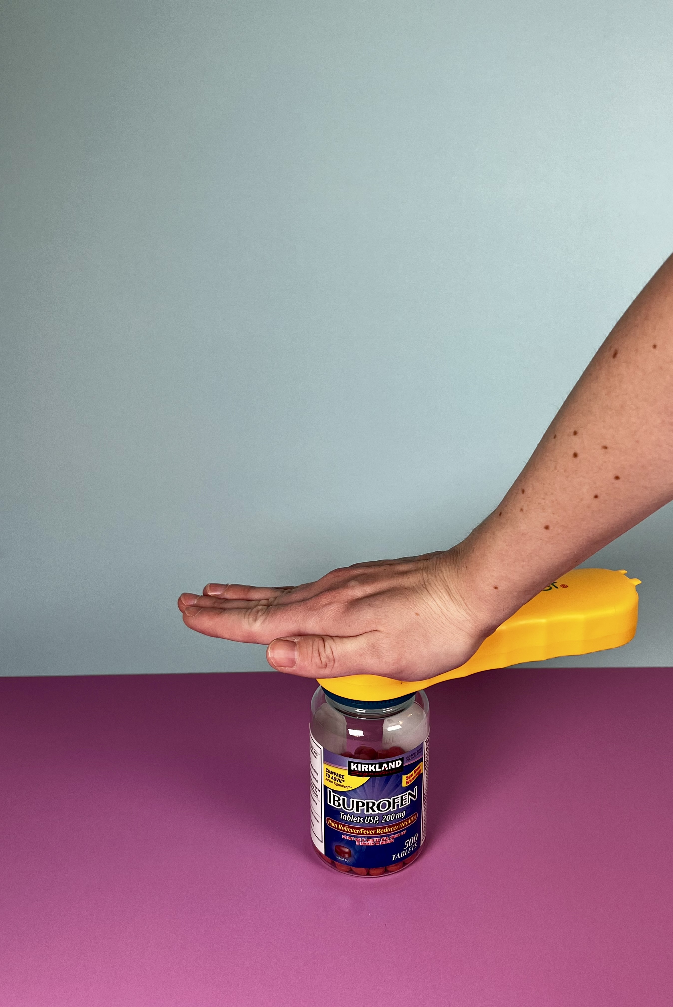 A hand pressing down on an orange easy-grip cap opener to open a medicine bottle.