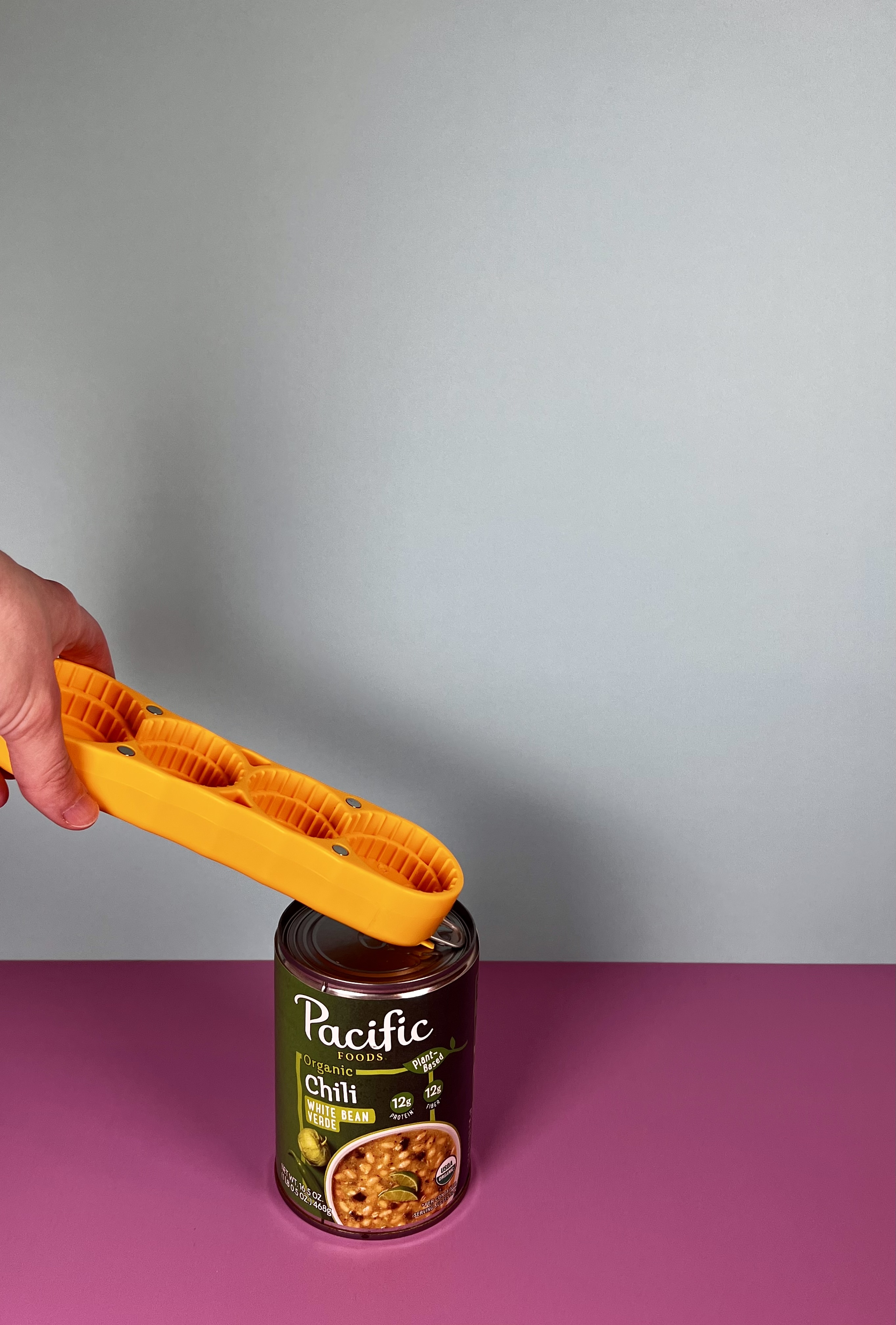 An orange easy-grip cap opener opening a can tab.