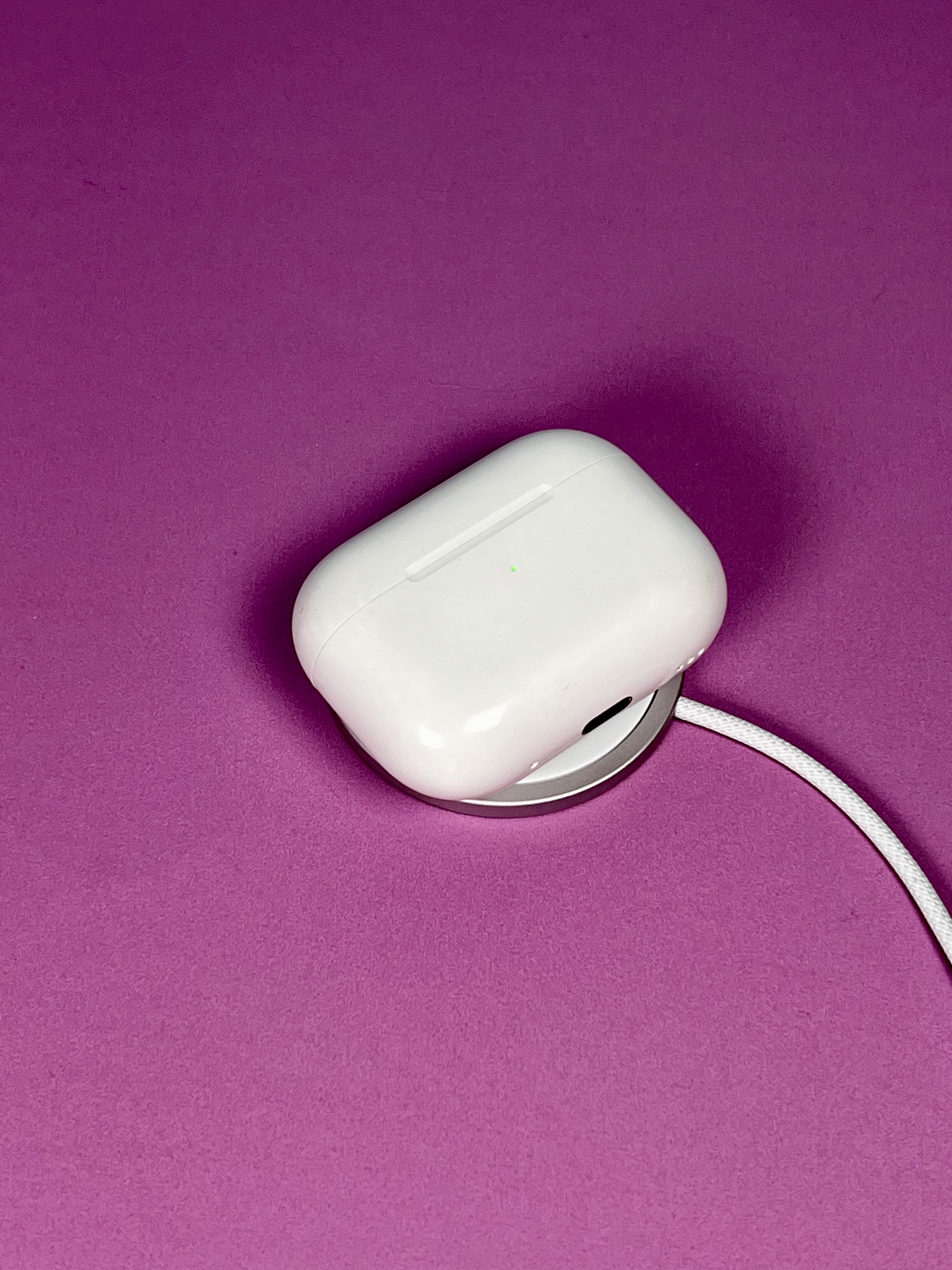 A white magnetic charging pad with a cable on a pink background.