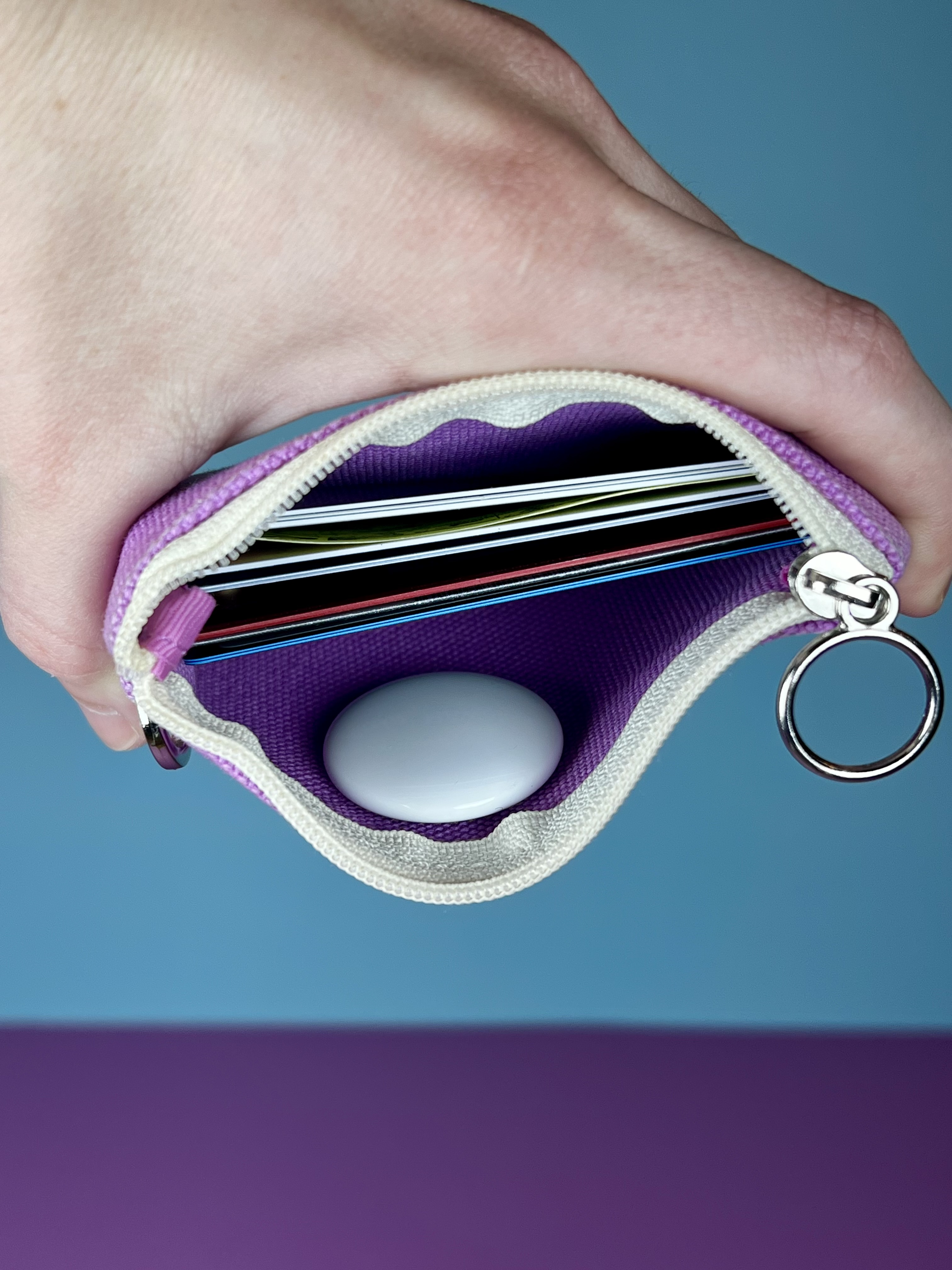 A hand opening a small pouch with a tracker inside to help keep track of items like a wallet, purse, keys, or remote.