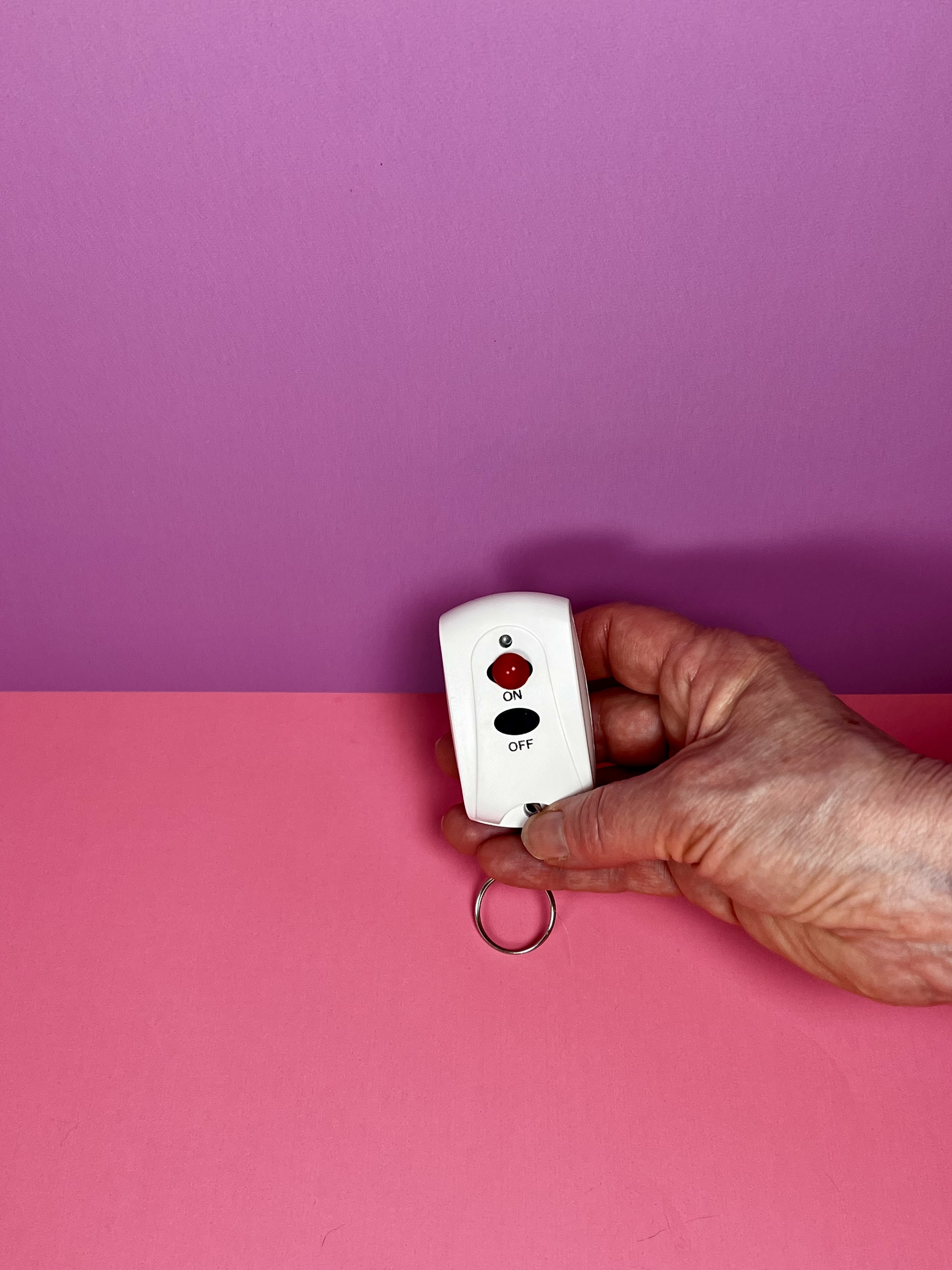 A hand holding a remote to control light switches with a red 3d dot on the "on" button
