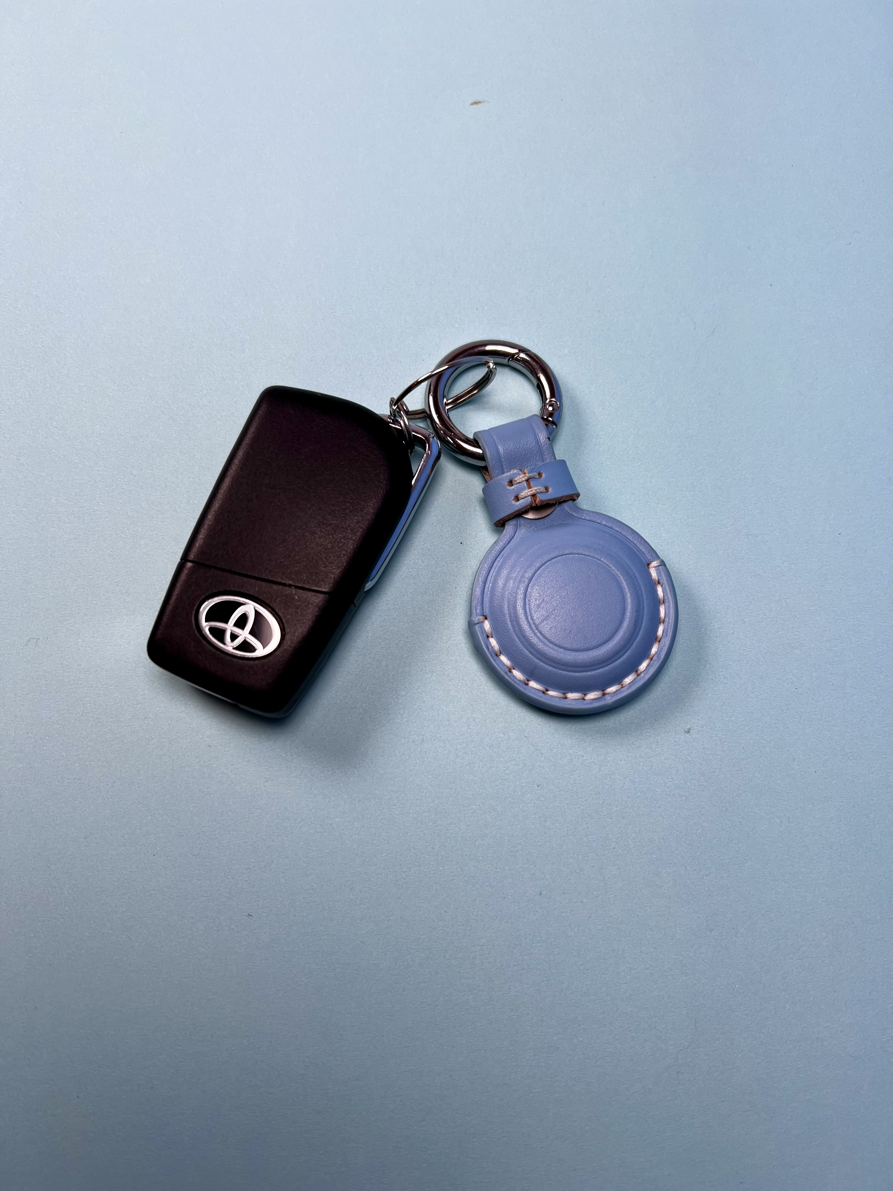 A keychain with a tracker holder attached to a set of keys on a blue background.