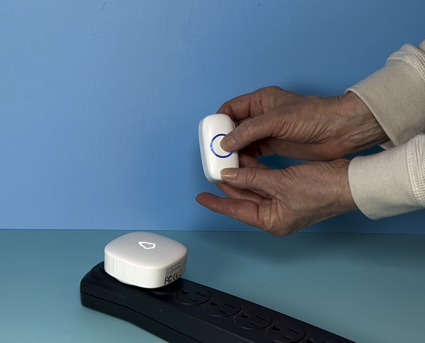 A hand holding a wireless doorbell button near its receiver on a blue background.