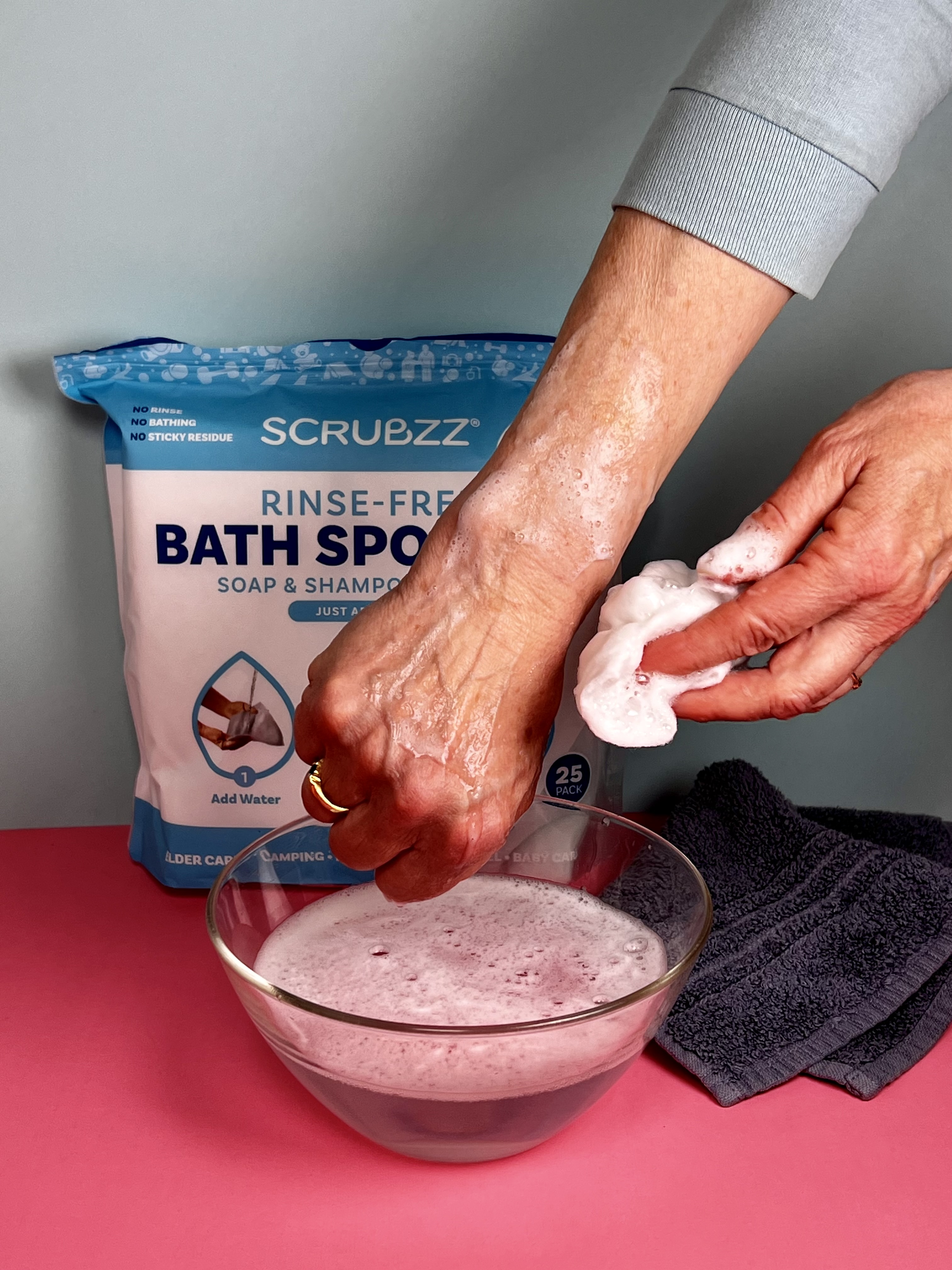 Hands squeezing a wet rinse-free bath sponge sheet over a bowl as it begins to foam.