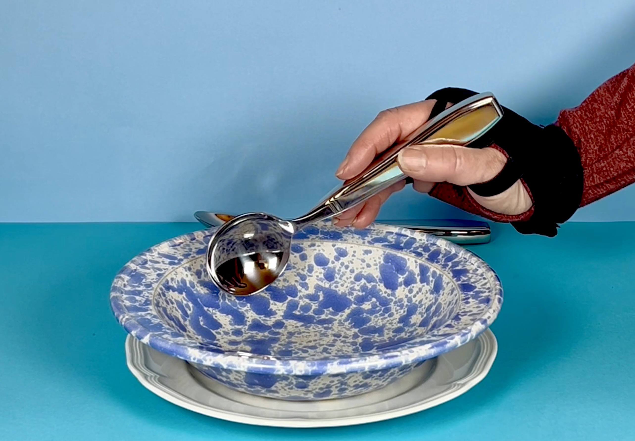 A hand with a weighted glove using a weighted spoon for tremor with a bowl