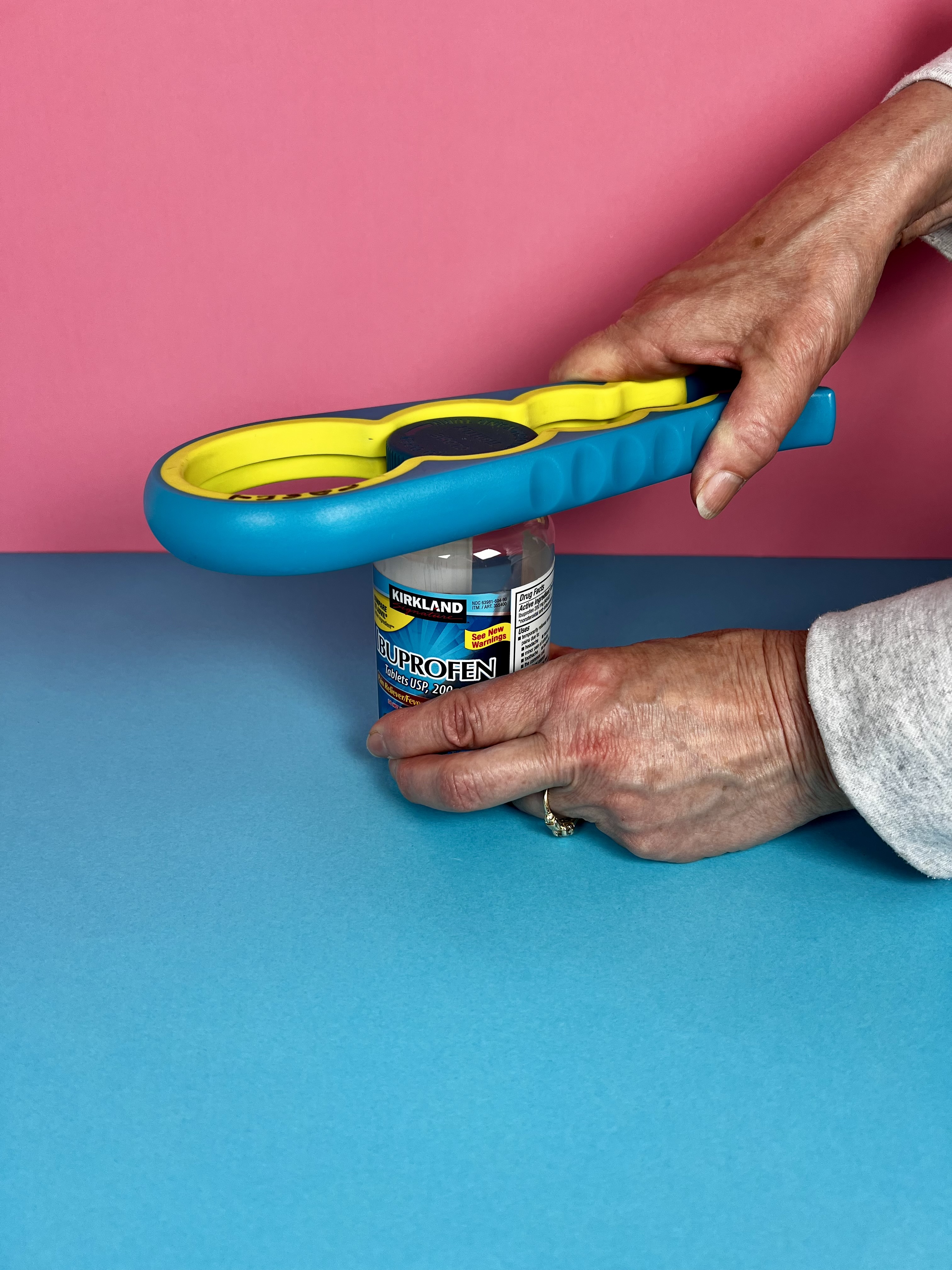 A hand using a colorful multi-size opener to twist the cap off a medicine bottle.