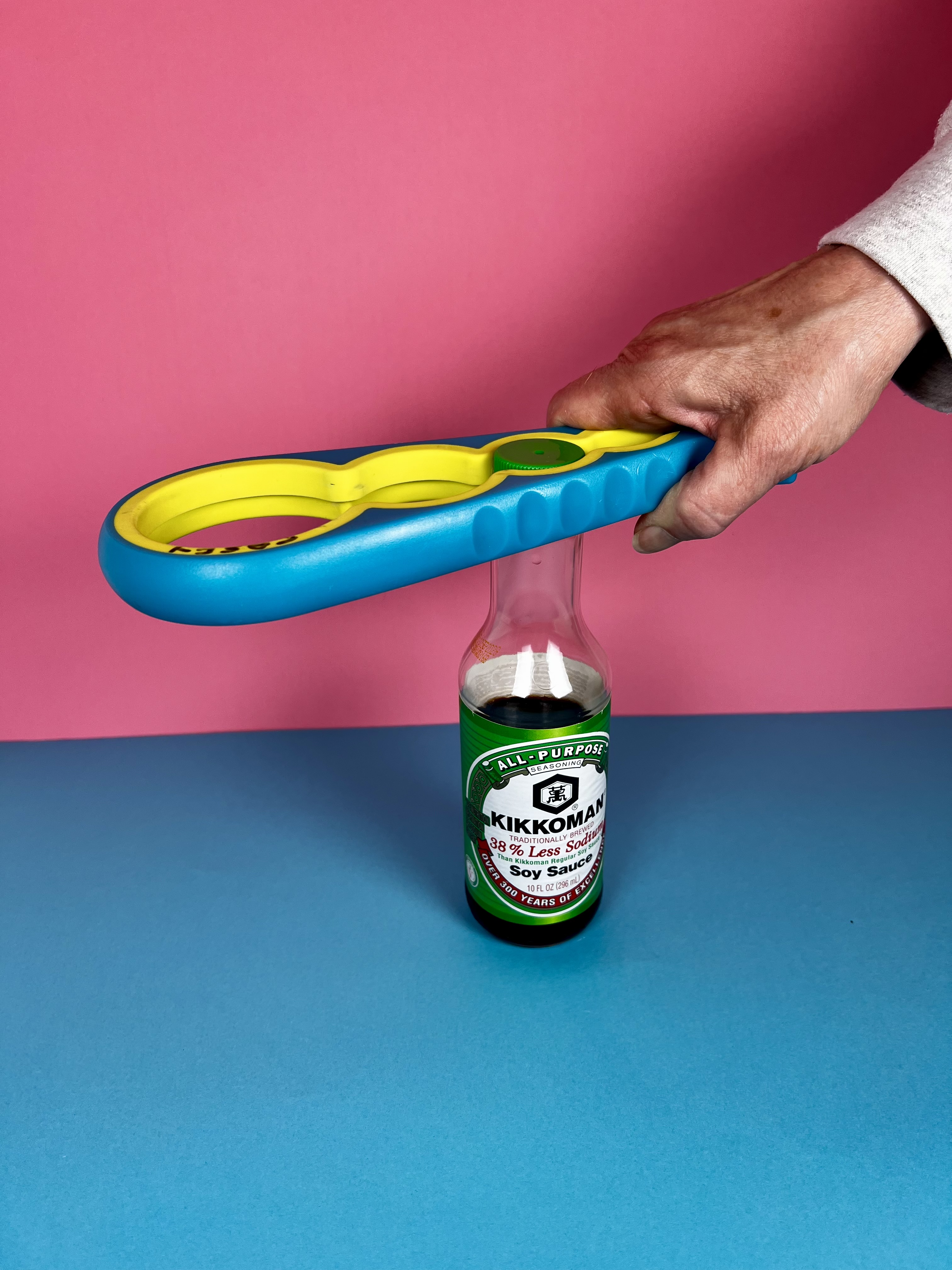 A hand positioning a colorful multi-size opener over a small condiment bottle cap.