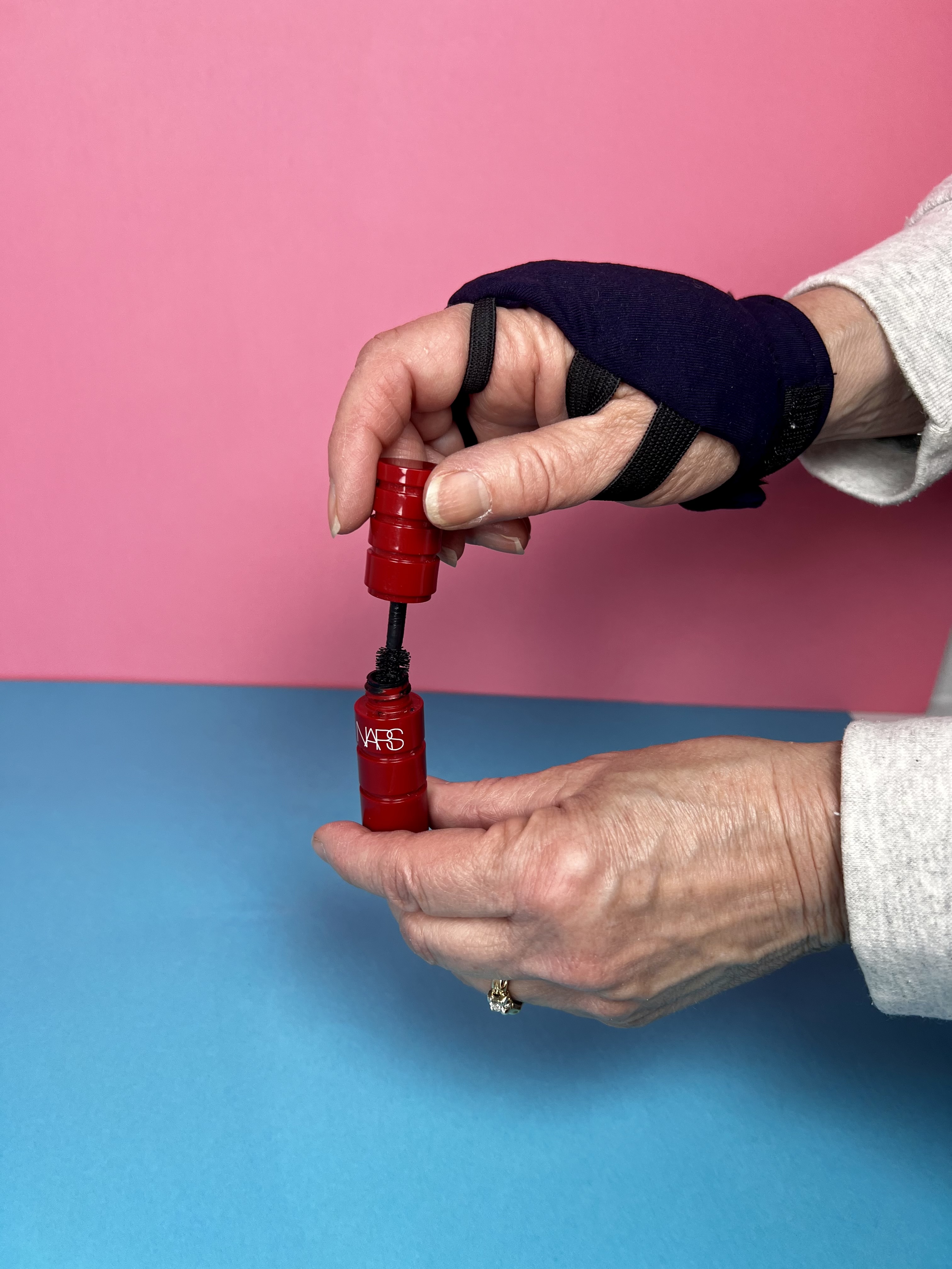 a hand in a weighted glove opening a mascara tube