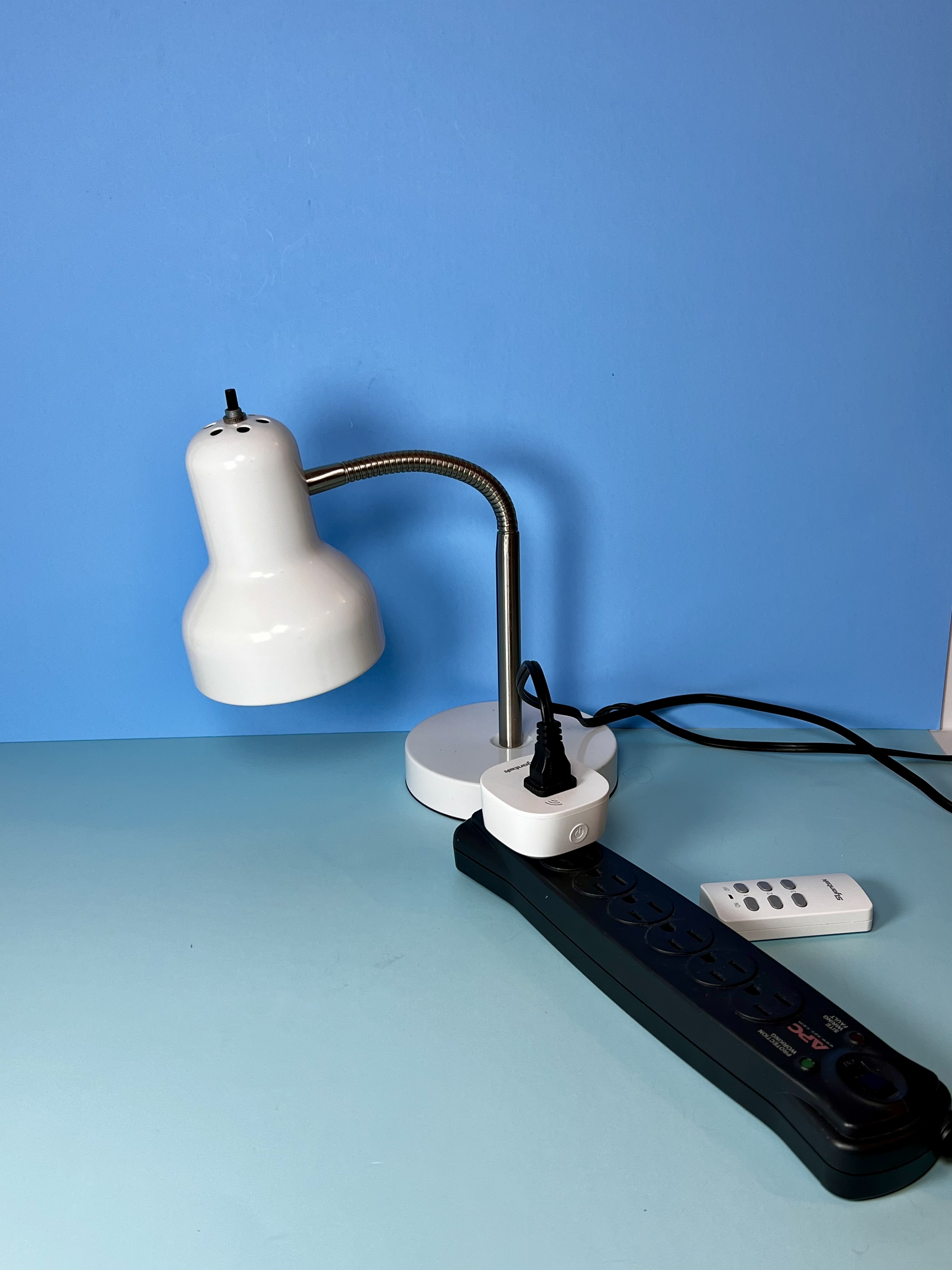 A lamp plugged into a white remote-control outlet with the handheld remote placed nearby.