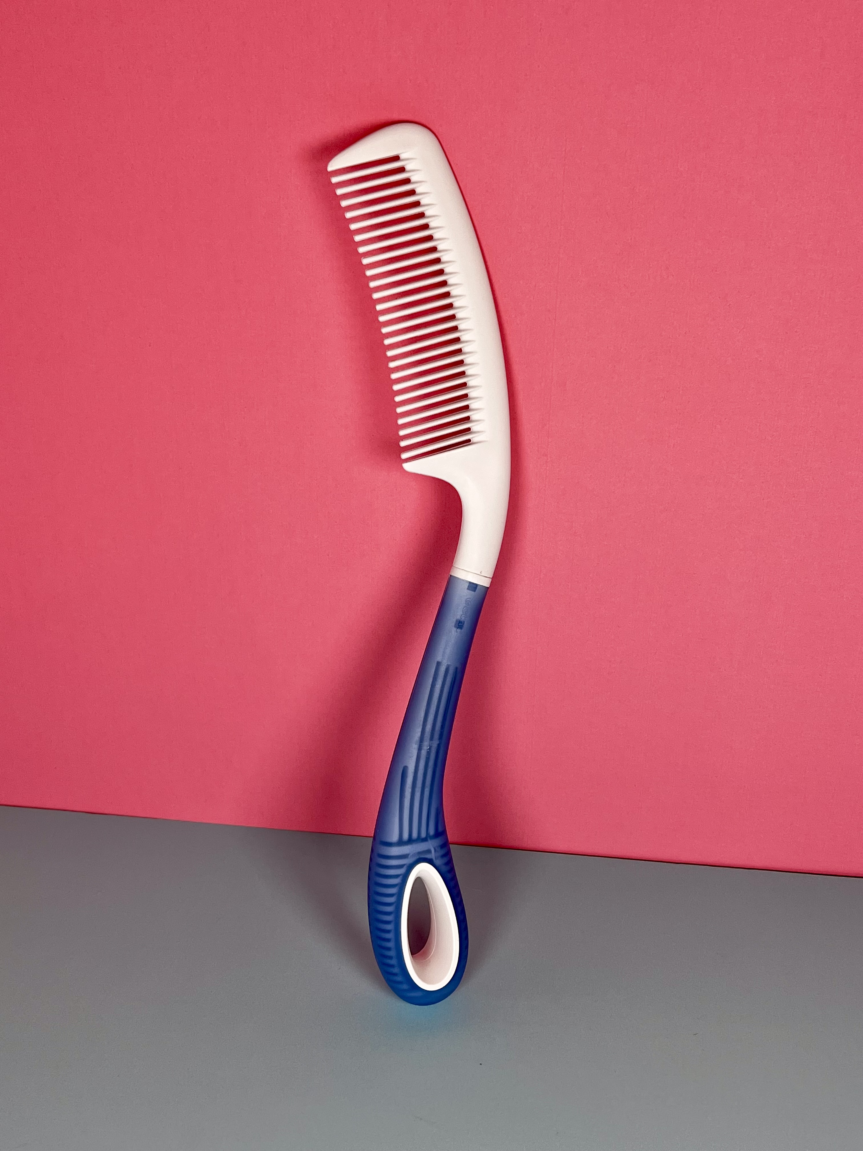 Pink background with long handled comb resting on the wall. 