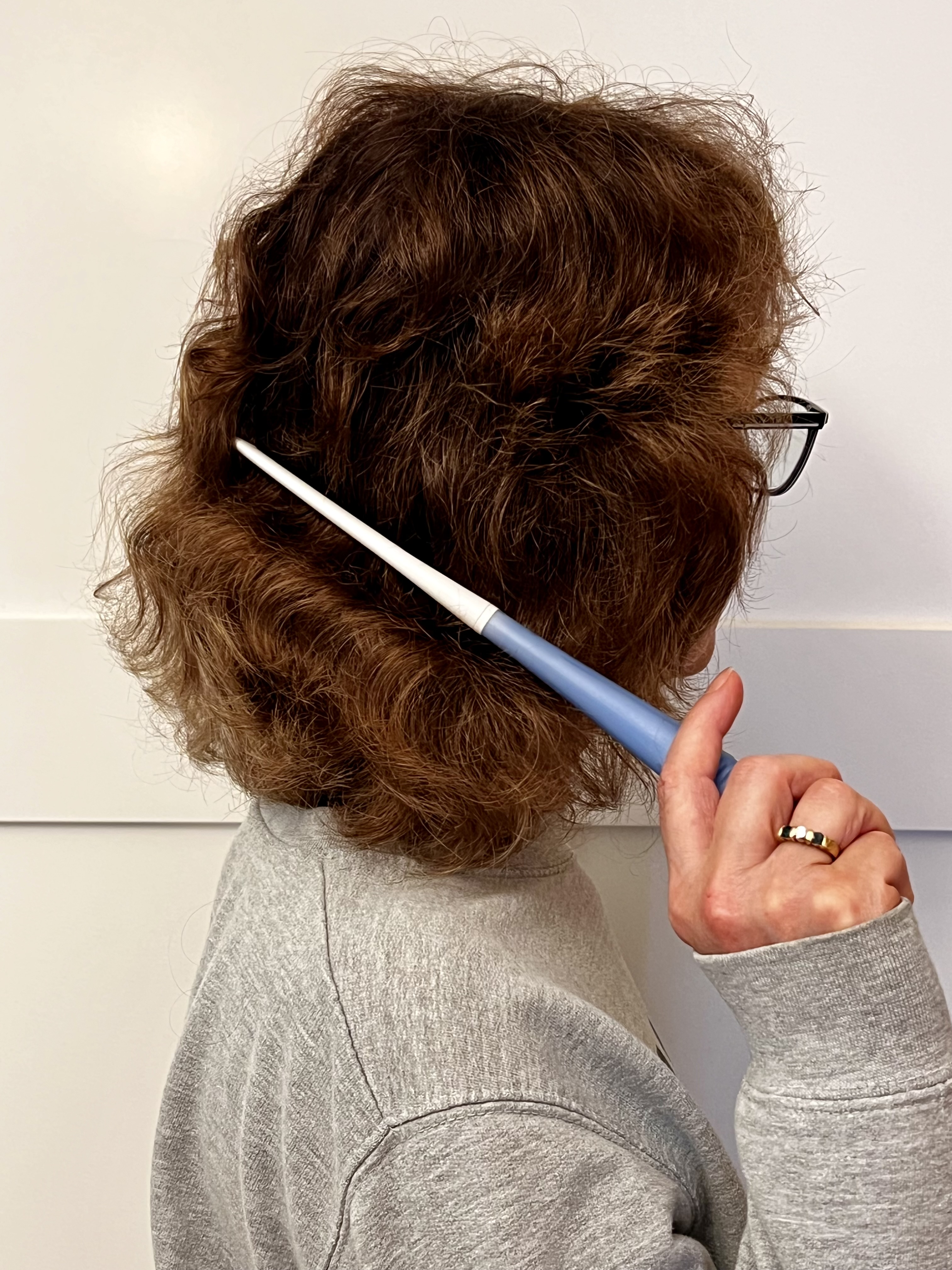 Side profile of woman combing the back of her hair with her arm and hand in front of her body. 