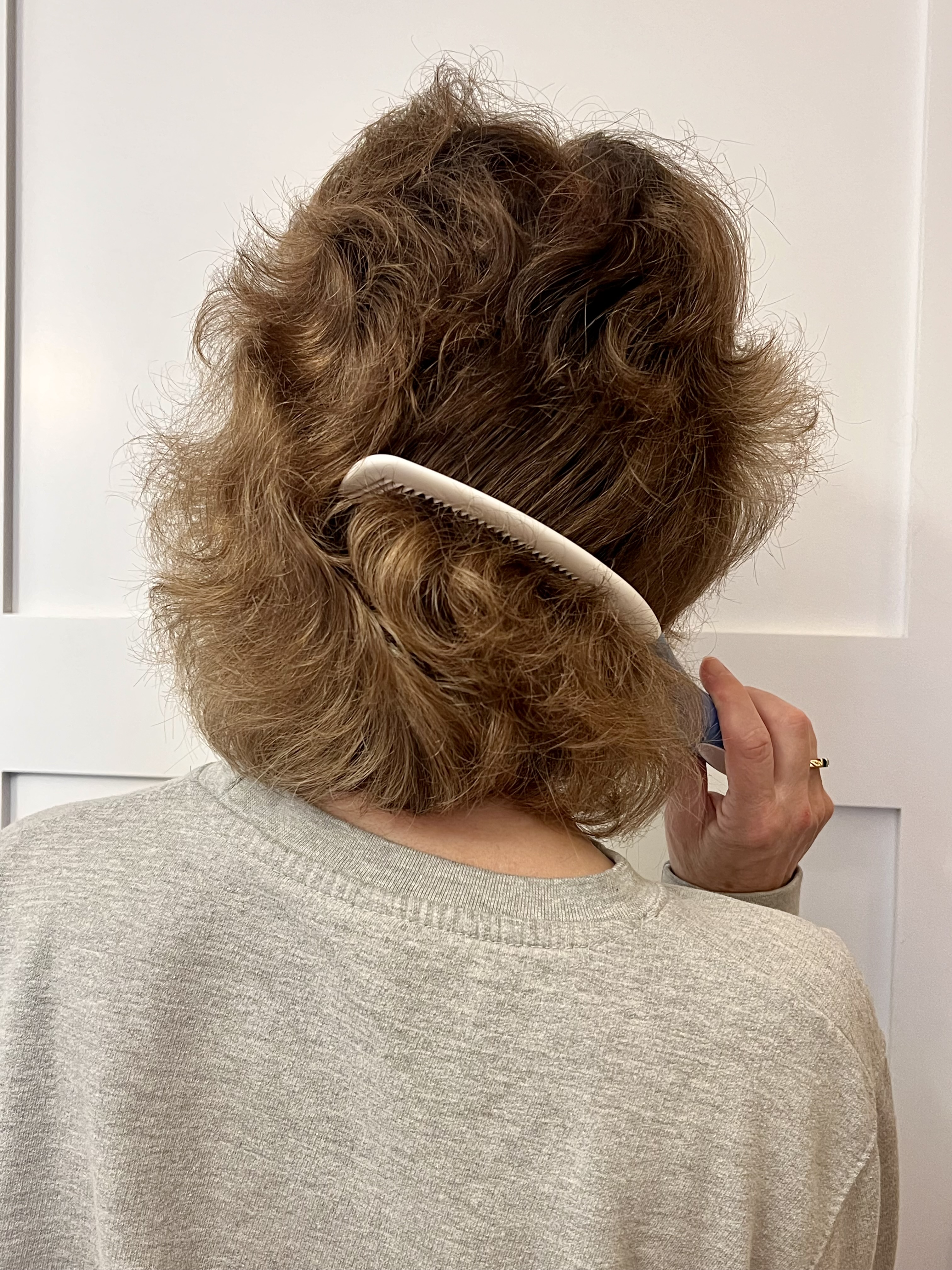 Shows the back of a woman with the comb reaching the back of her hair while her arm remains in the front of her body.
