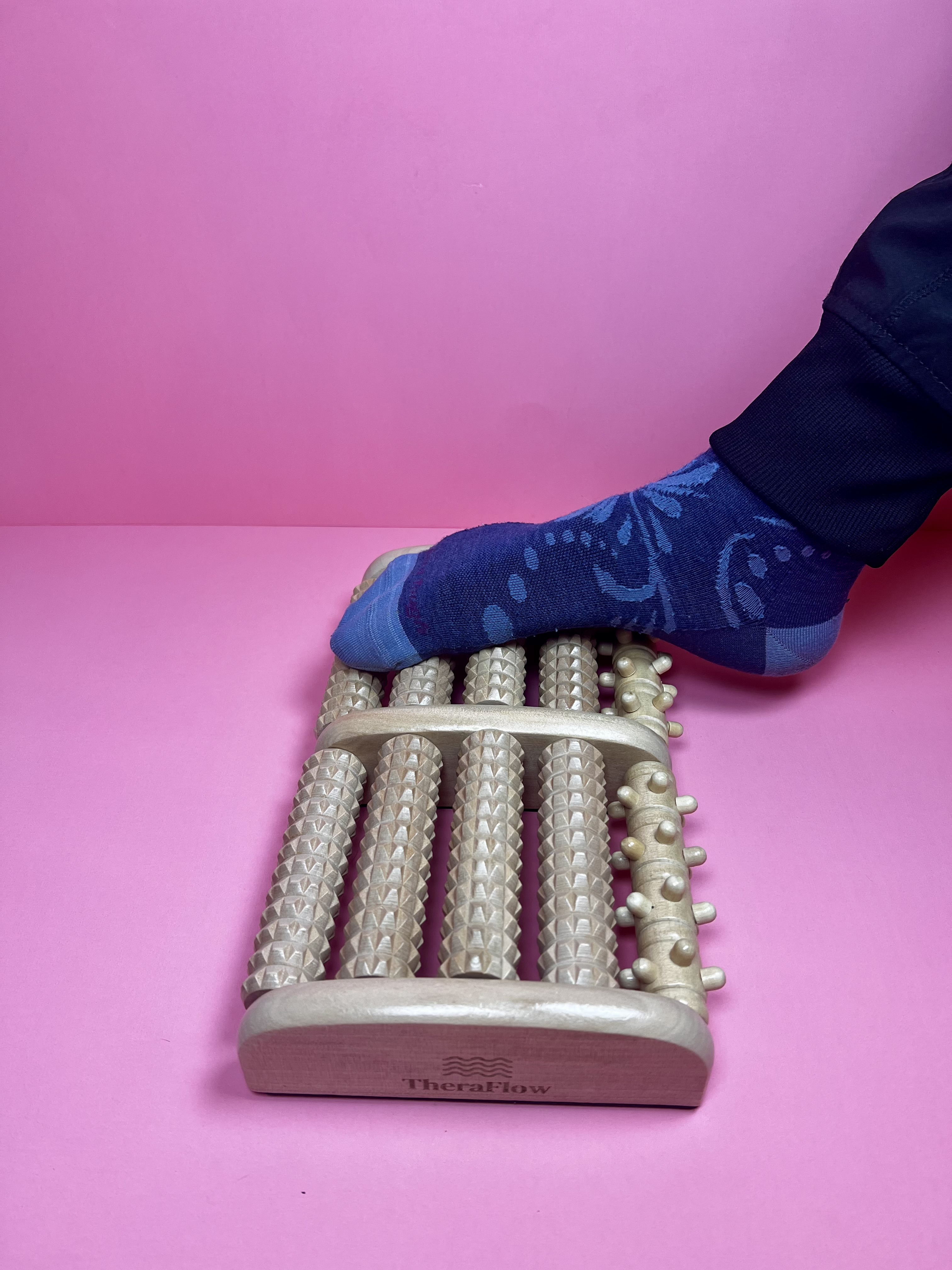 Person using a wooden foot roller massager while seated.