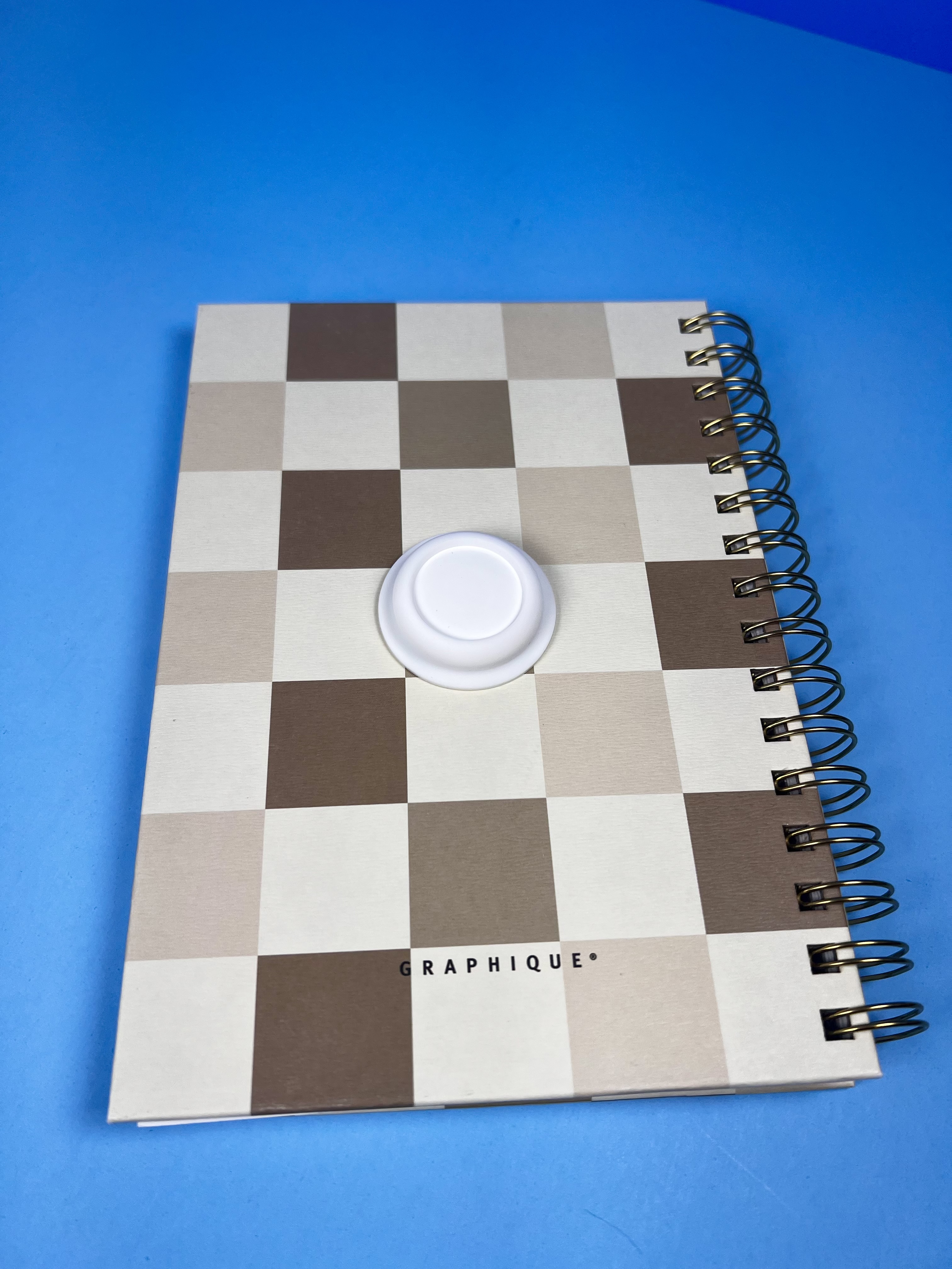 White AirTag attached to the front of a spiral notebook.