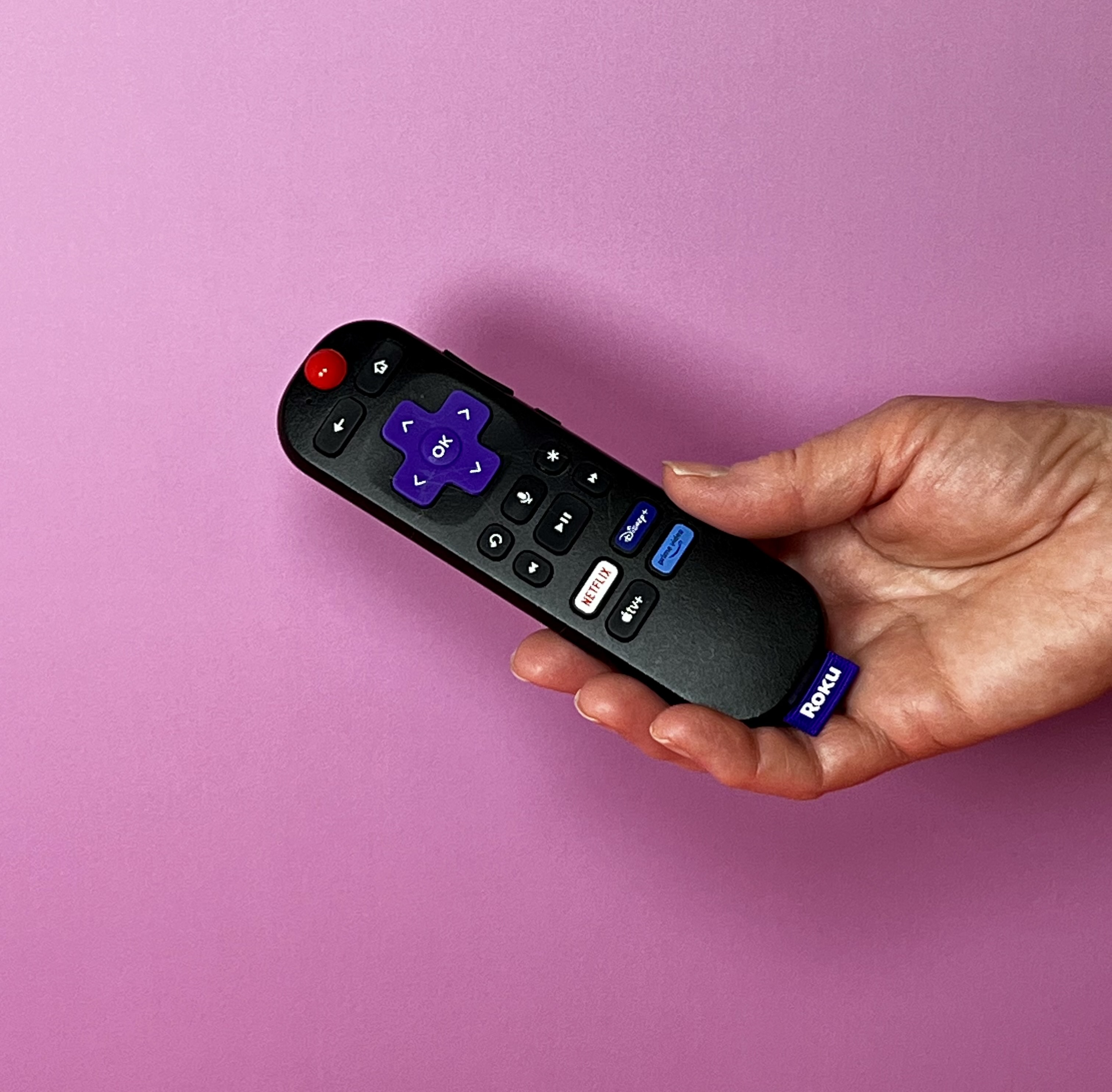 A hand holds a Roku remote with a red tactile marker placed on the power button.
