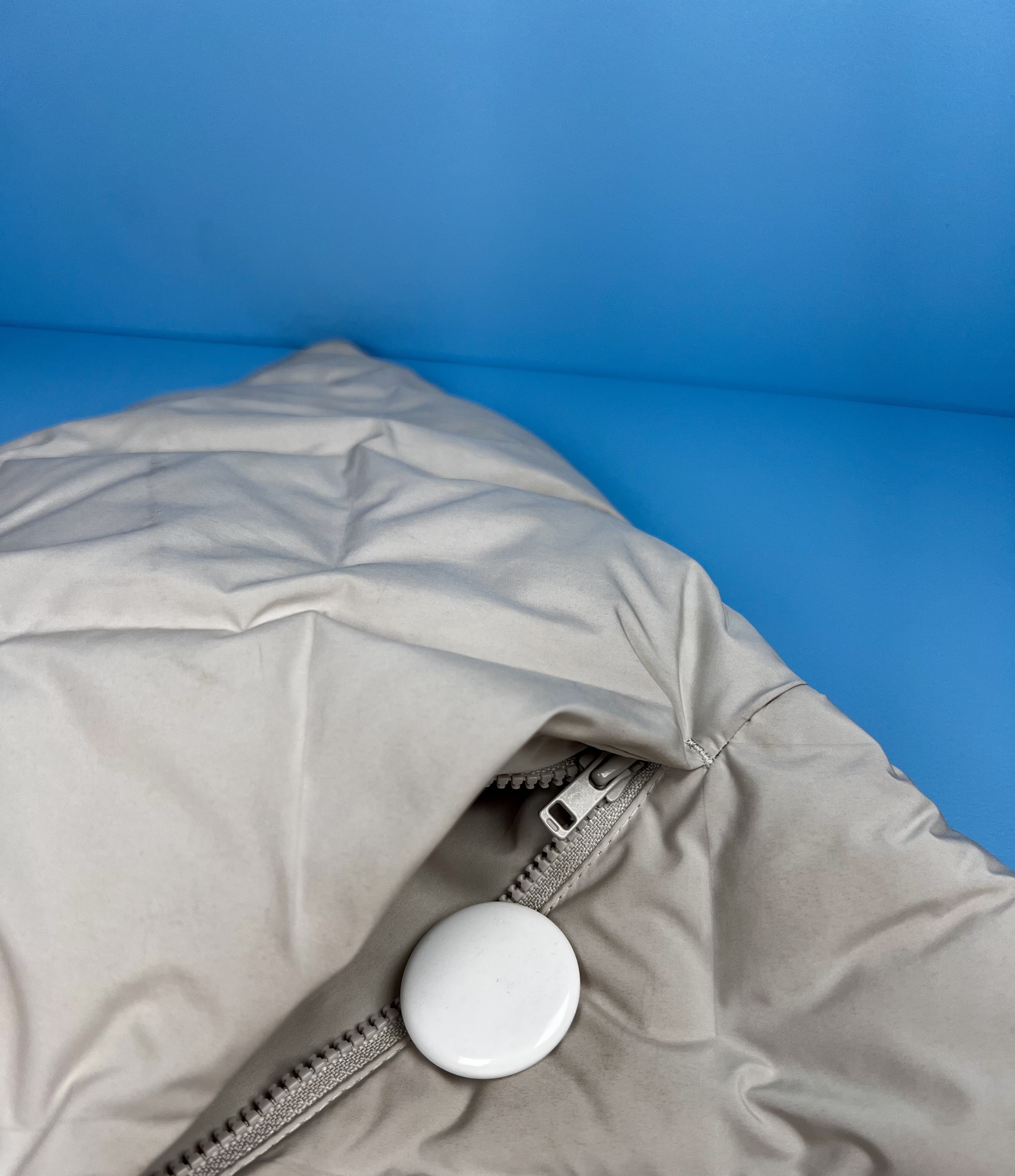 White AirTag placed inside the zippered pocket of a jacket.
