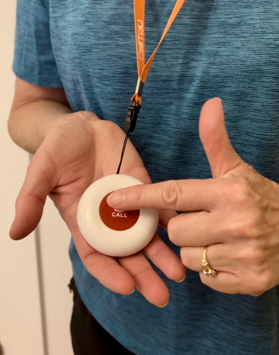 Person wearing a caregiver call button on a lanyard and pressing the red call button.