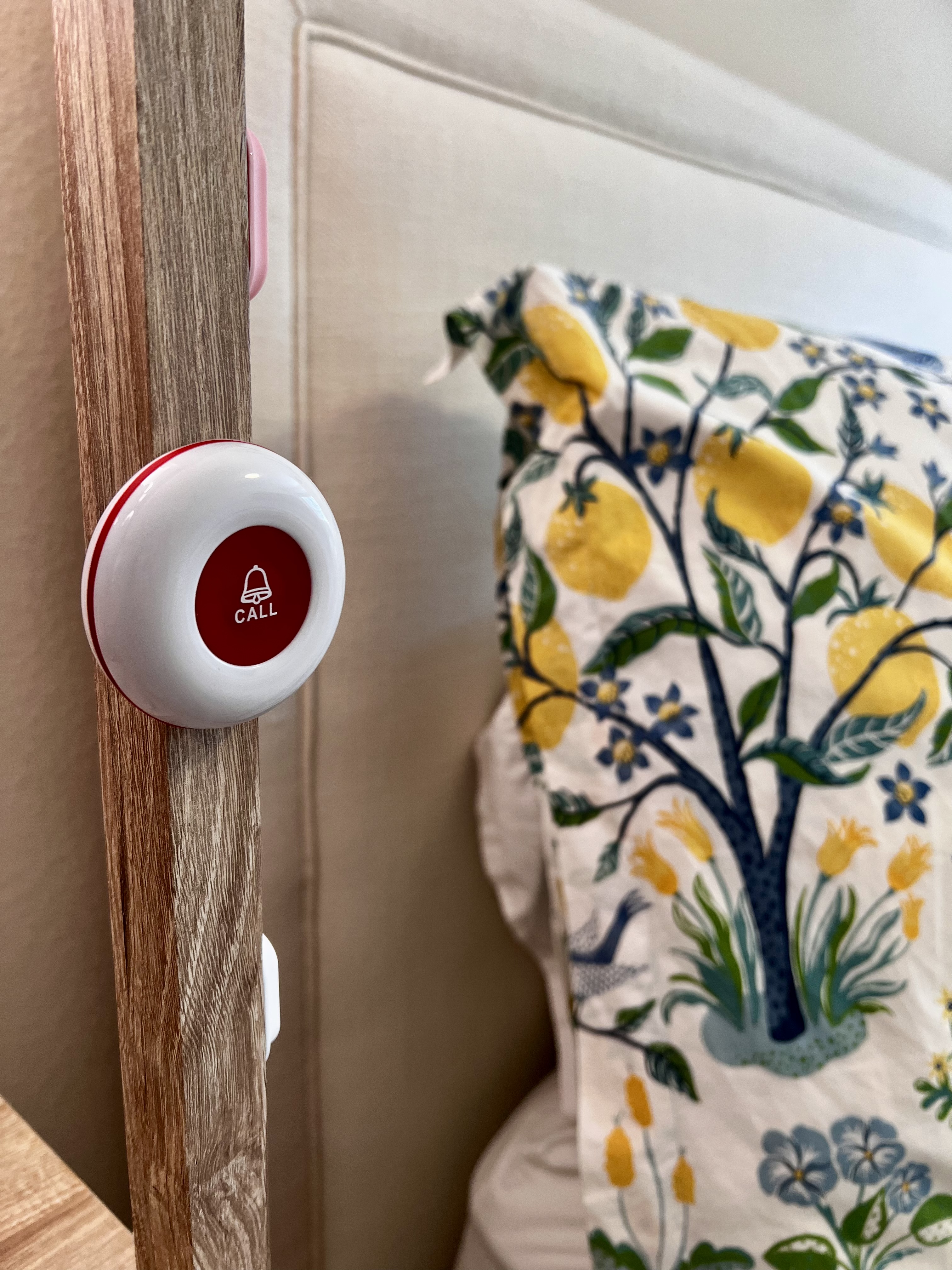 Caregiver call button mounted on a wooden bed frame beside a pillow.