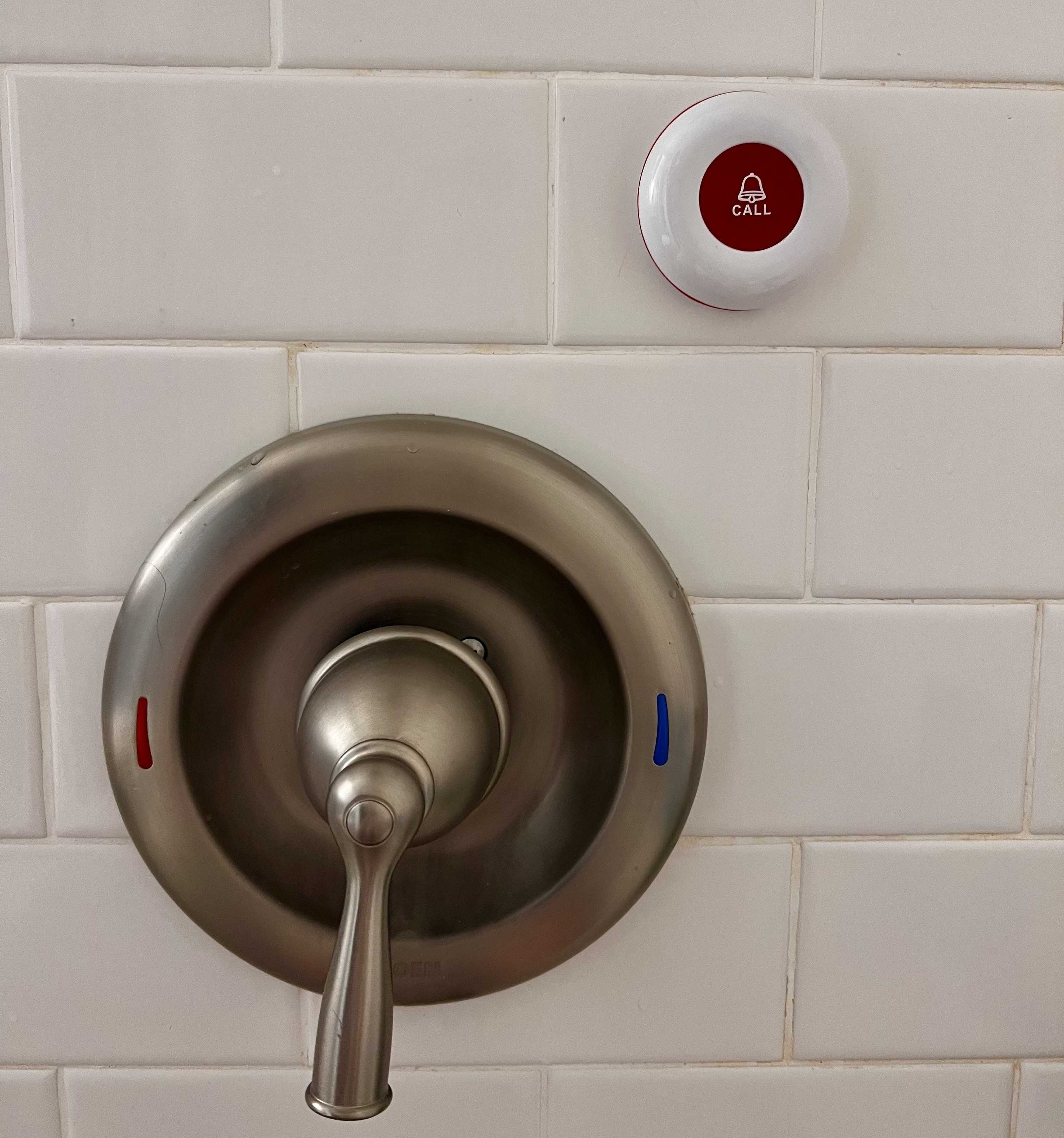 Caregiver call button mounted on the shower wall above the faucet handle.