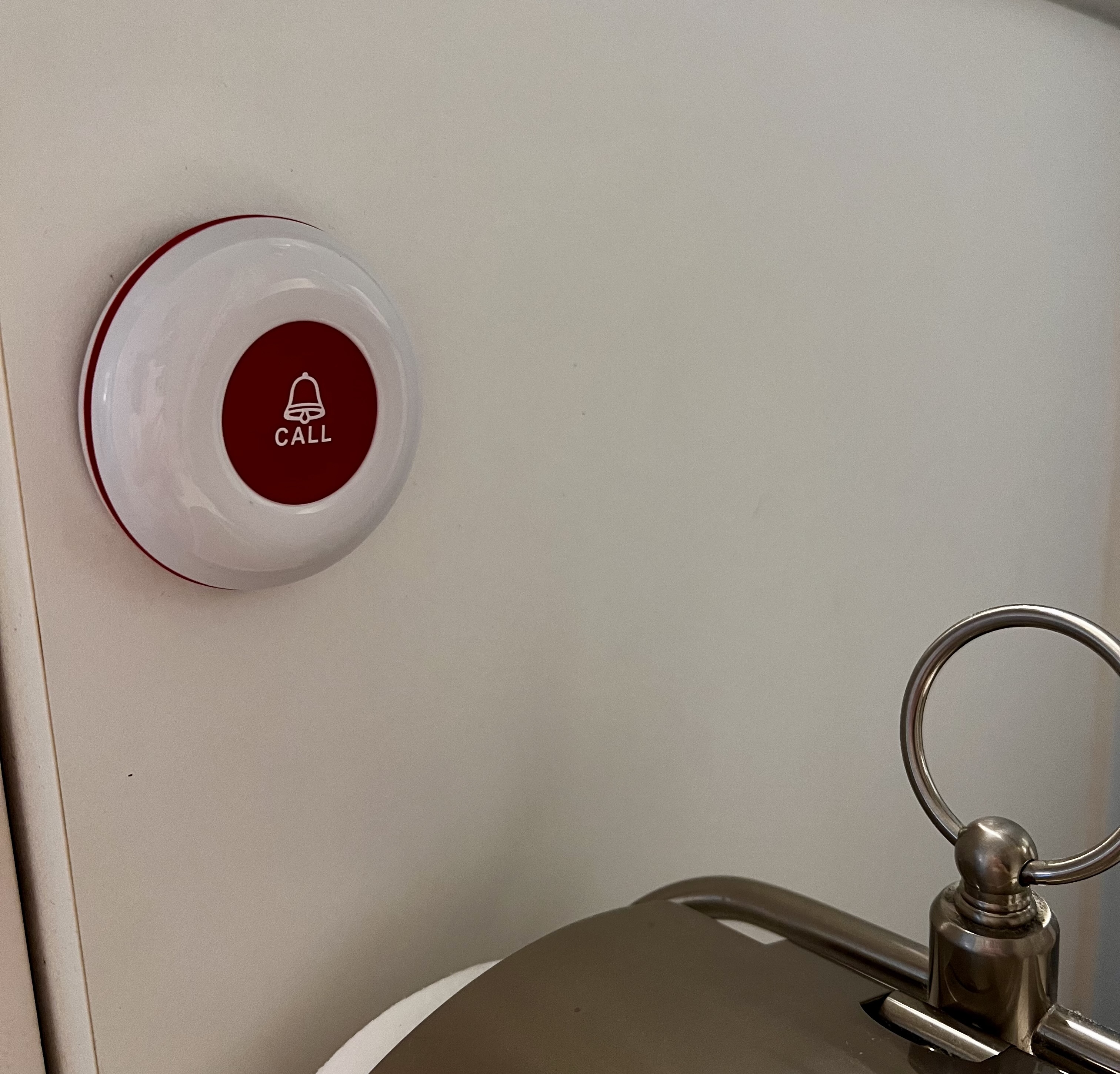 Caregiver call button mounted on the wall beside a toilet.