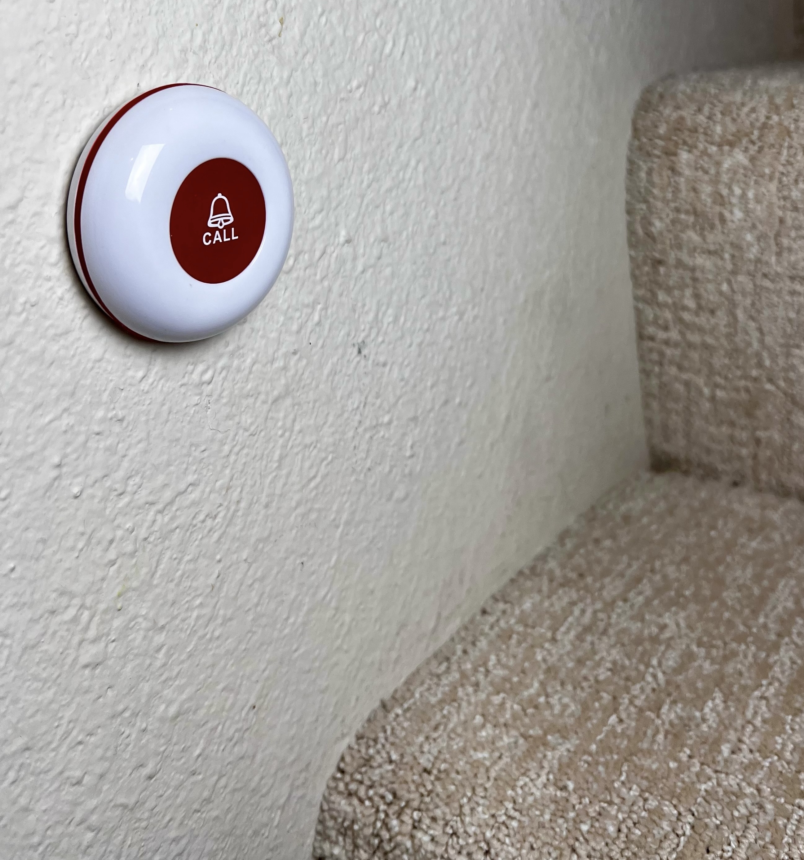 Caregiver call button mounted low on the wall beside a carpeted staircase.