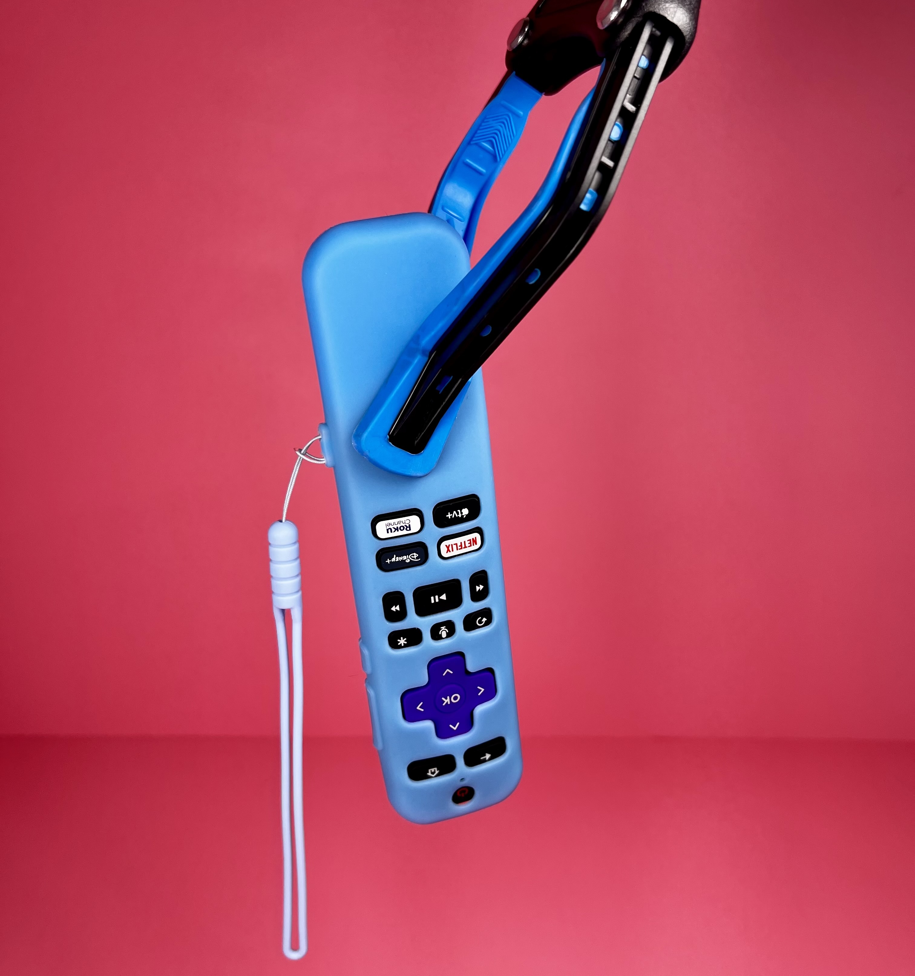 Reacher grabber tool holding a blue TV remote against a pink background.