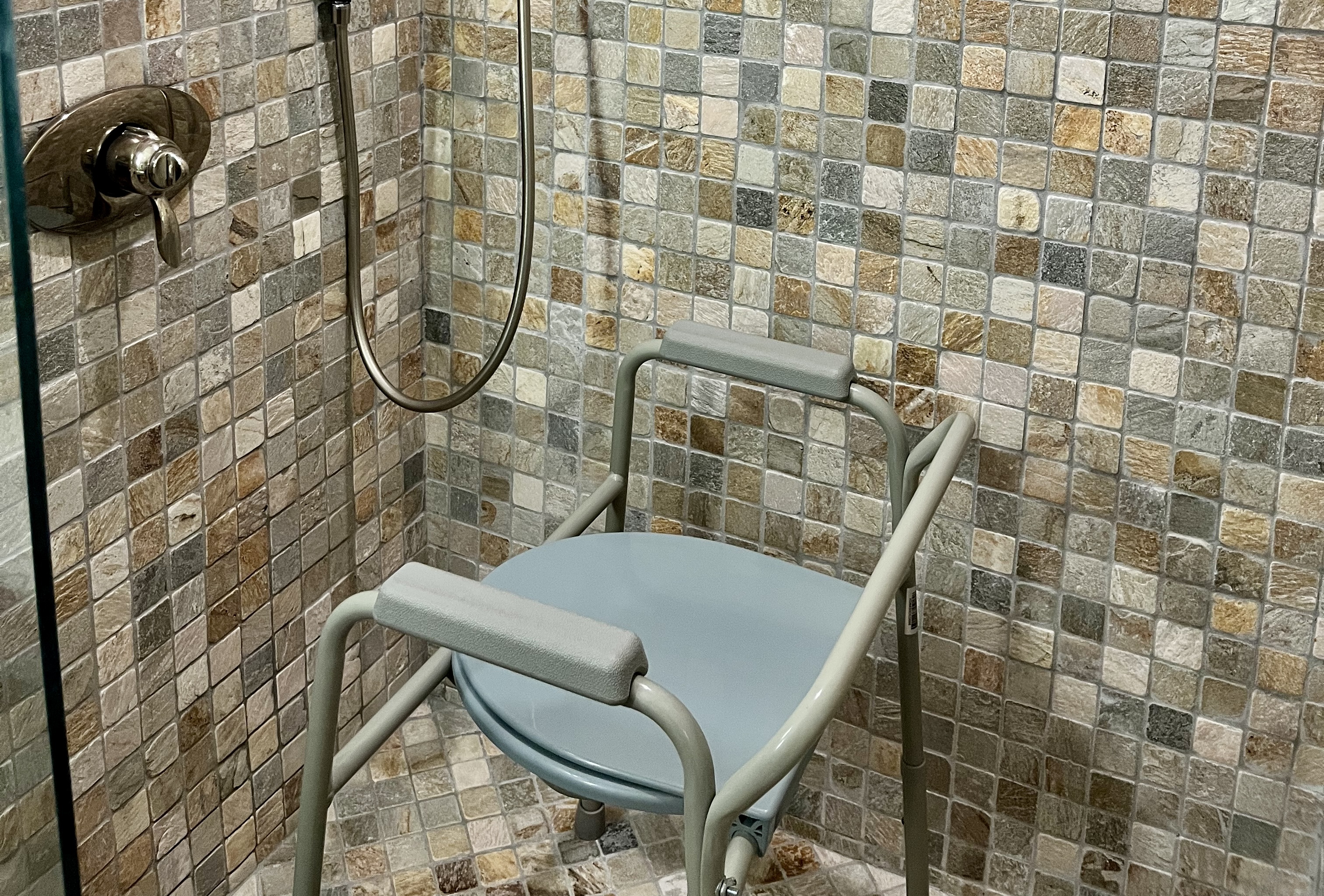 Padded shower chair with armrests and a backrest positioned inside a tiled shower.
