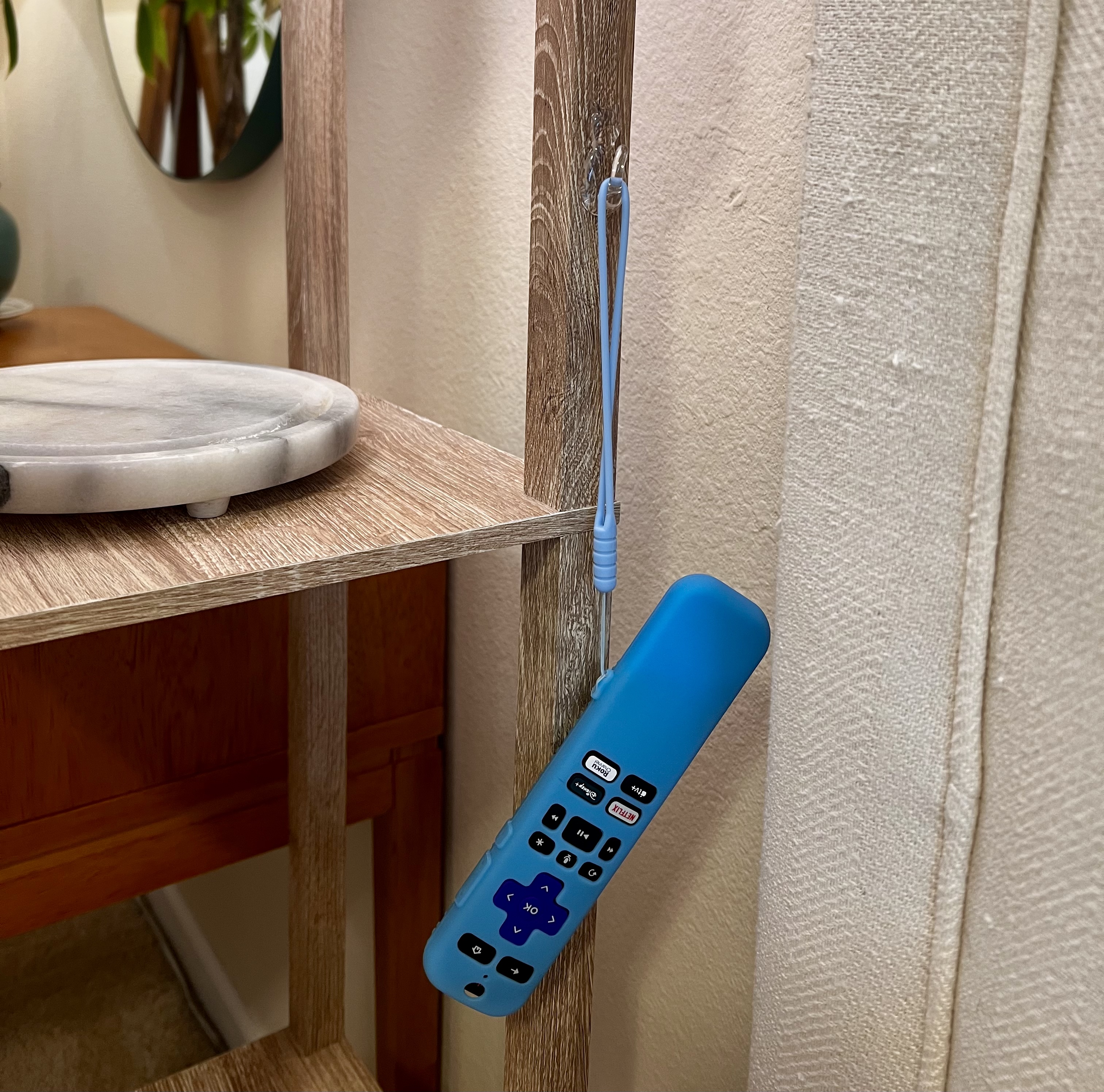 Blue Roku remote hanging from a wooden shelf by its wrist strap for easy access.