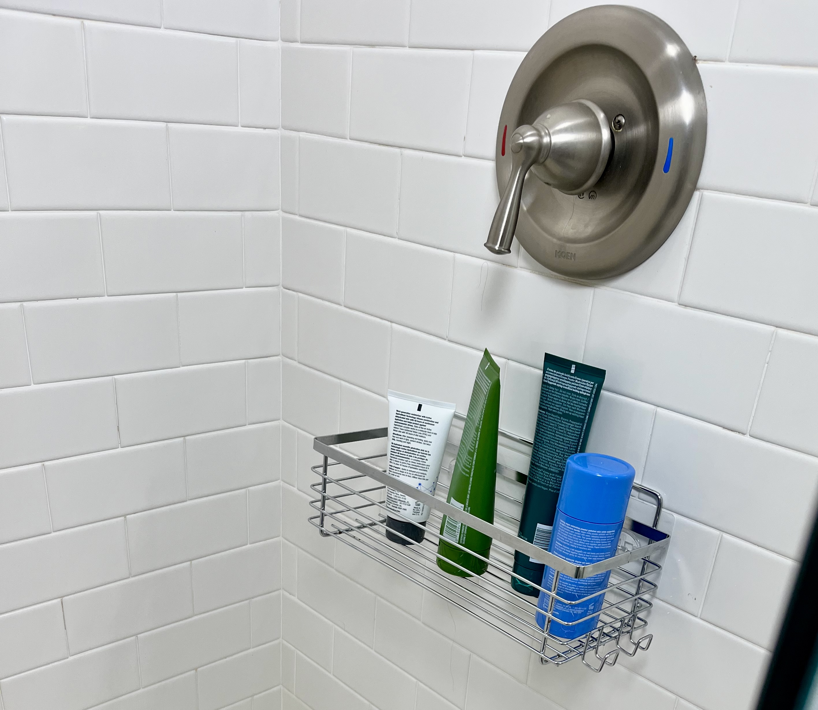 Metal shower caddy mounted below the faucet controls, holding toiletries within easy reach.
