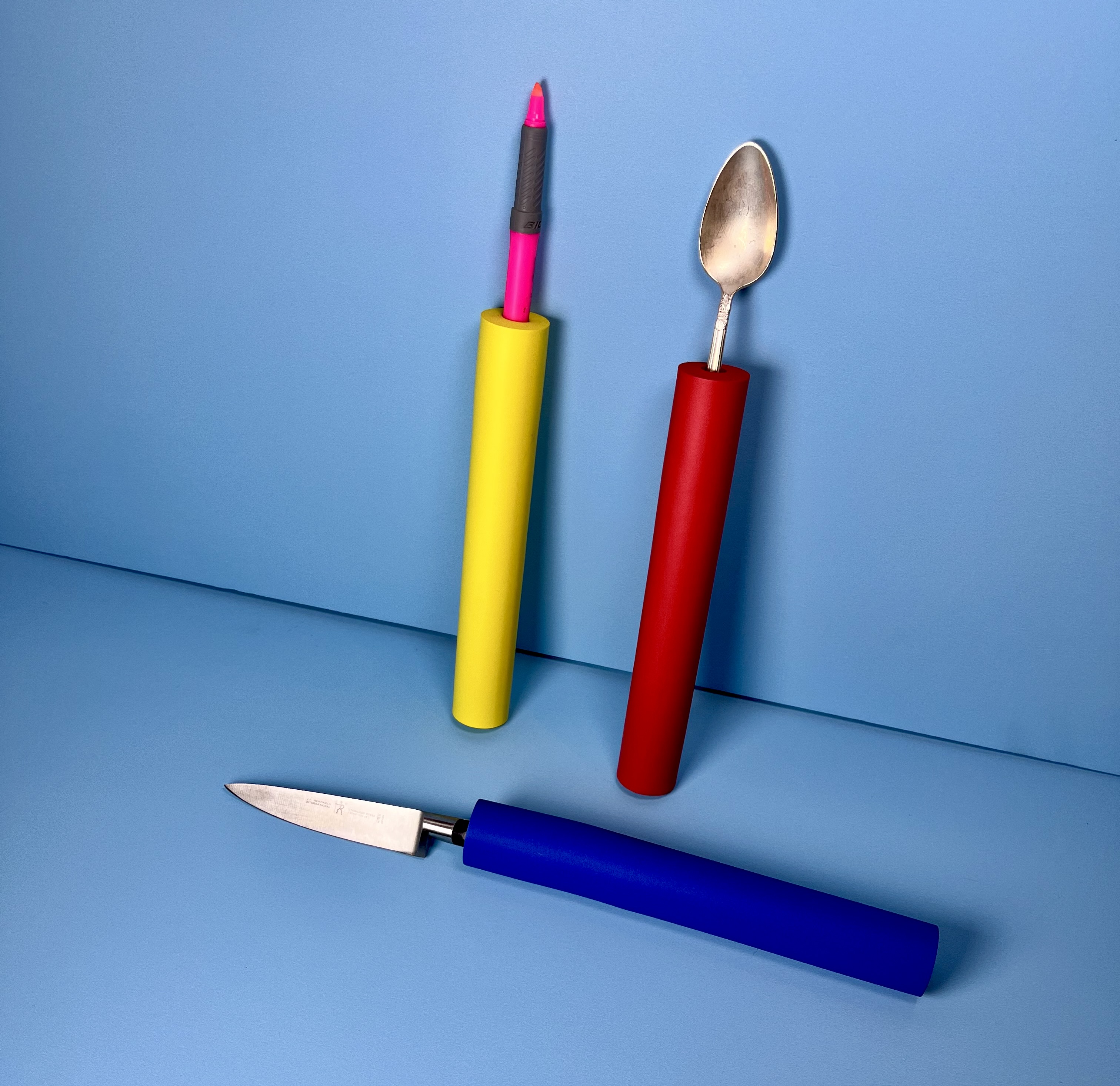 Colorful foam tubes are fitted over a pen, spoon, and knife handles to create thicker grips.