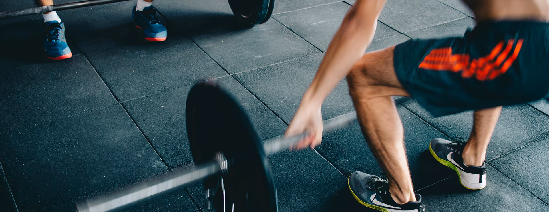 Person lifting a heavy barbell on a gym floor with rubber mats.