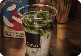 Clear cup of iced matcha latte with green tea pouring over milk on wooden table.