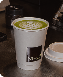 Cup of green matcha latte with latte art in a white cup labeled Niroo on a counter.