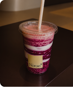 Plastic cup with layered pink and white smoothie labeled Niroo with a straw on a dark surface.