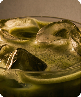 Close-up of a glass with green drink and large ice cubes inside.