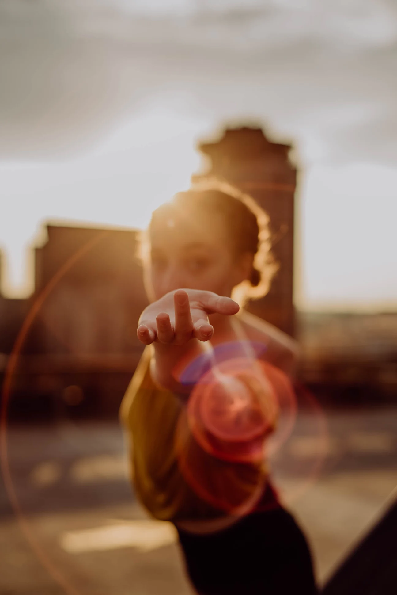 Person extending hand towards the camera with the sun shining behind in an outdoor setting.