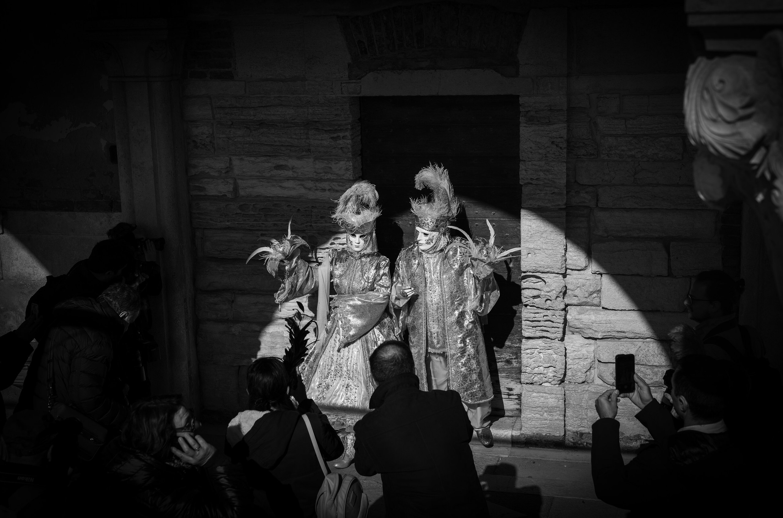 Venetian carnival costumes in a spotlight, photographed by a crowd
